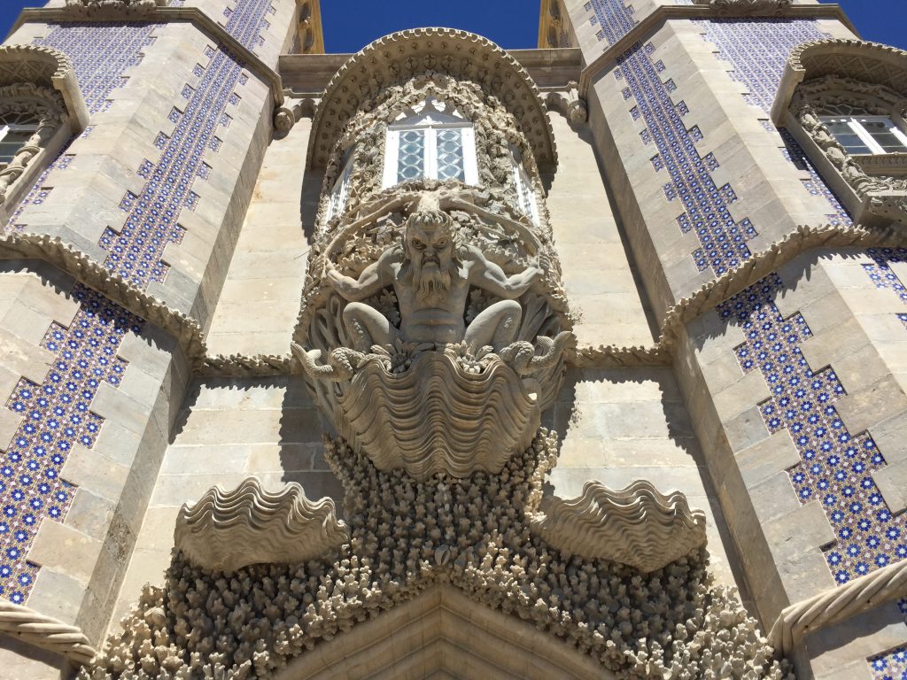 Detailed stone carving of a mythological sea god at Pena Palace, Sintra, Portugal, surrounded by blue azulejos tiles.