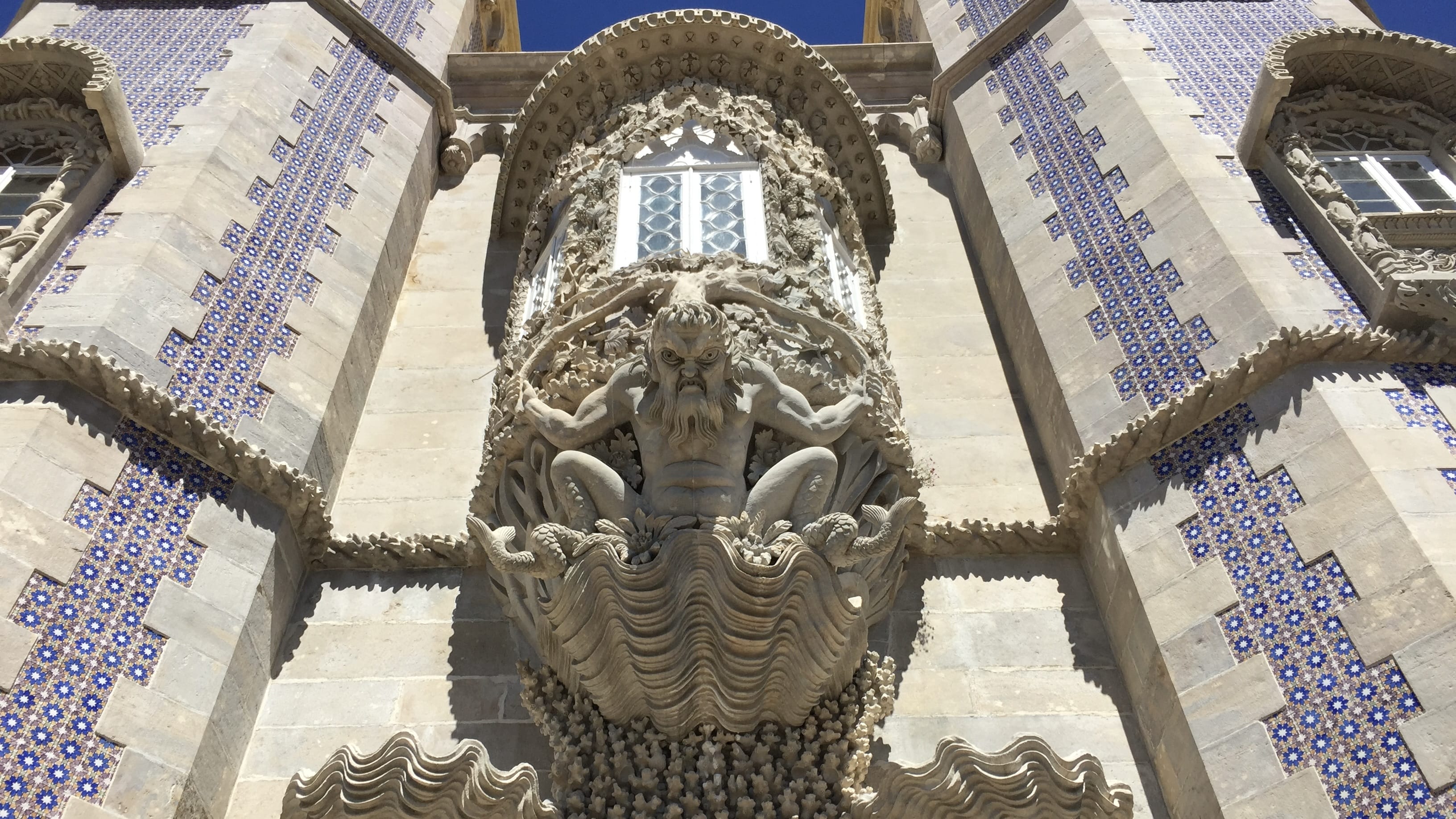 Detailed stone carving of a mythological sea god at Pena Palace, Sintra, Portugal, surrounded by blue azulejos tiles.
