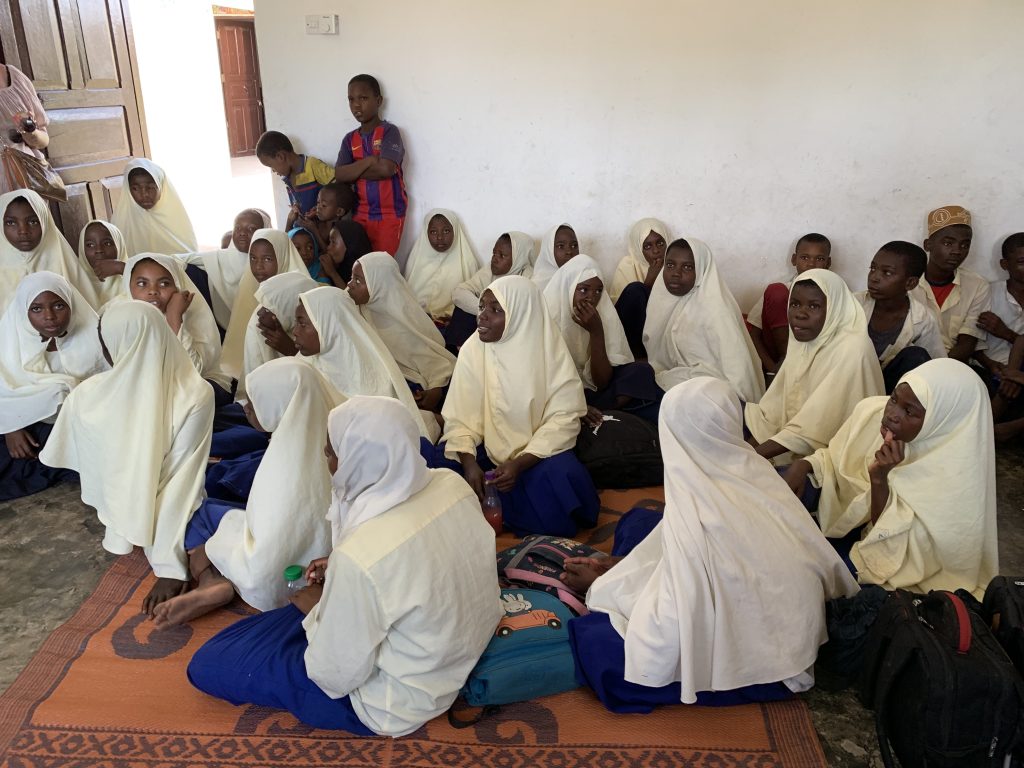 Classroom of Muslim girls in white hijabs seated on a mat, listening attentively in Zanzibar