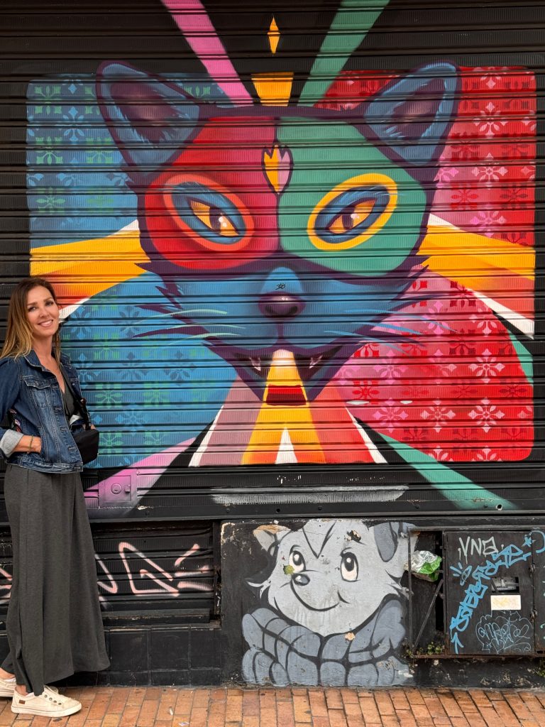 Woman standing beside a colorful cat-themed mural on a shutter door in Bogotá, Colombia.