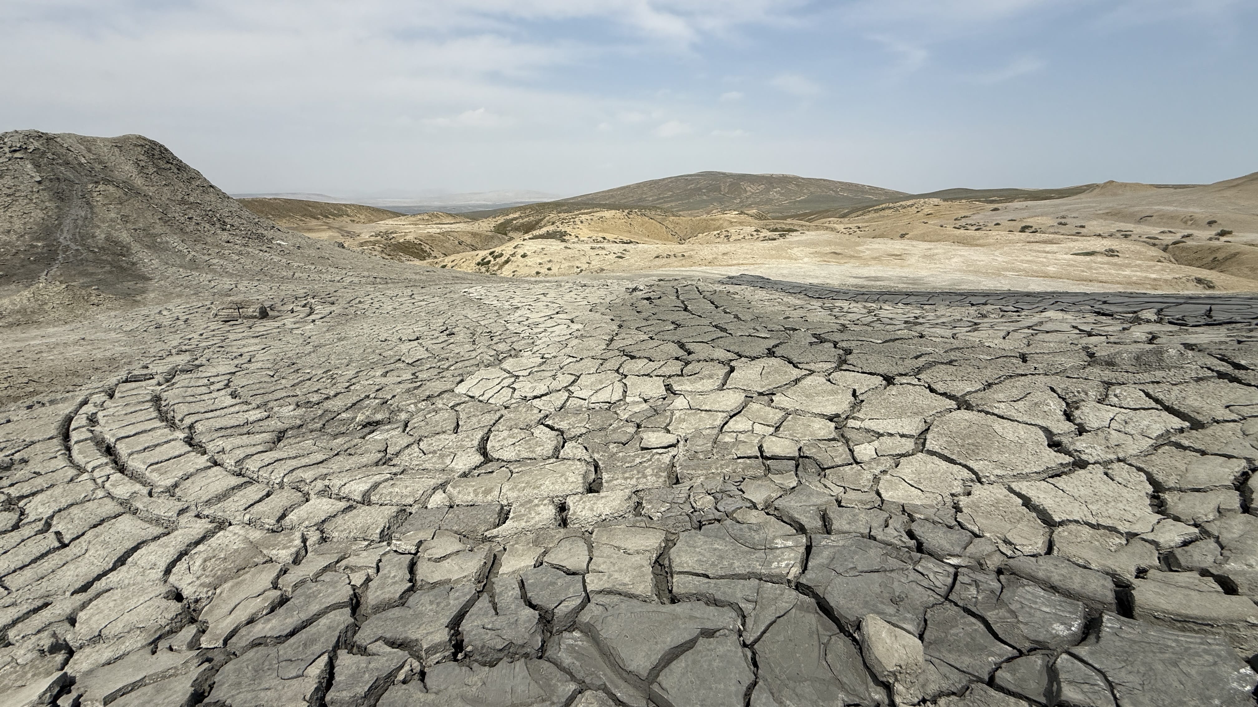 Expansive view of the cracked gray surface and rolling hills of the Gobustan mud volcano area in Azerbaijan.