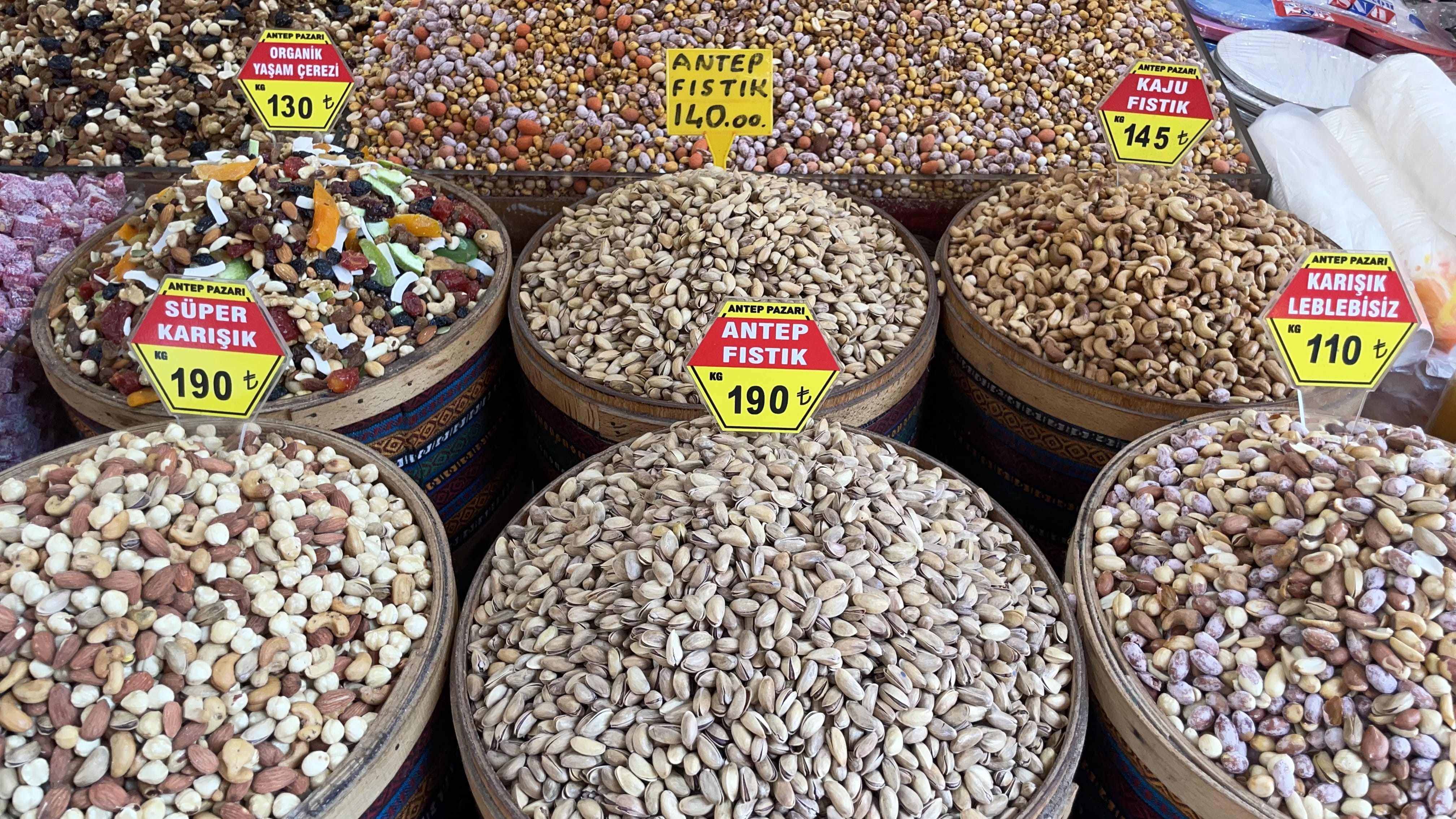 Assorted nuts and dried fruit for sale in large wooden barrels at a market in Istanbul, including pistachios, cashews, and mixed trail blends — popular vegetarian snacks in Turkey.
