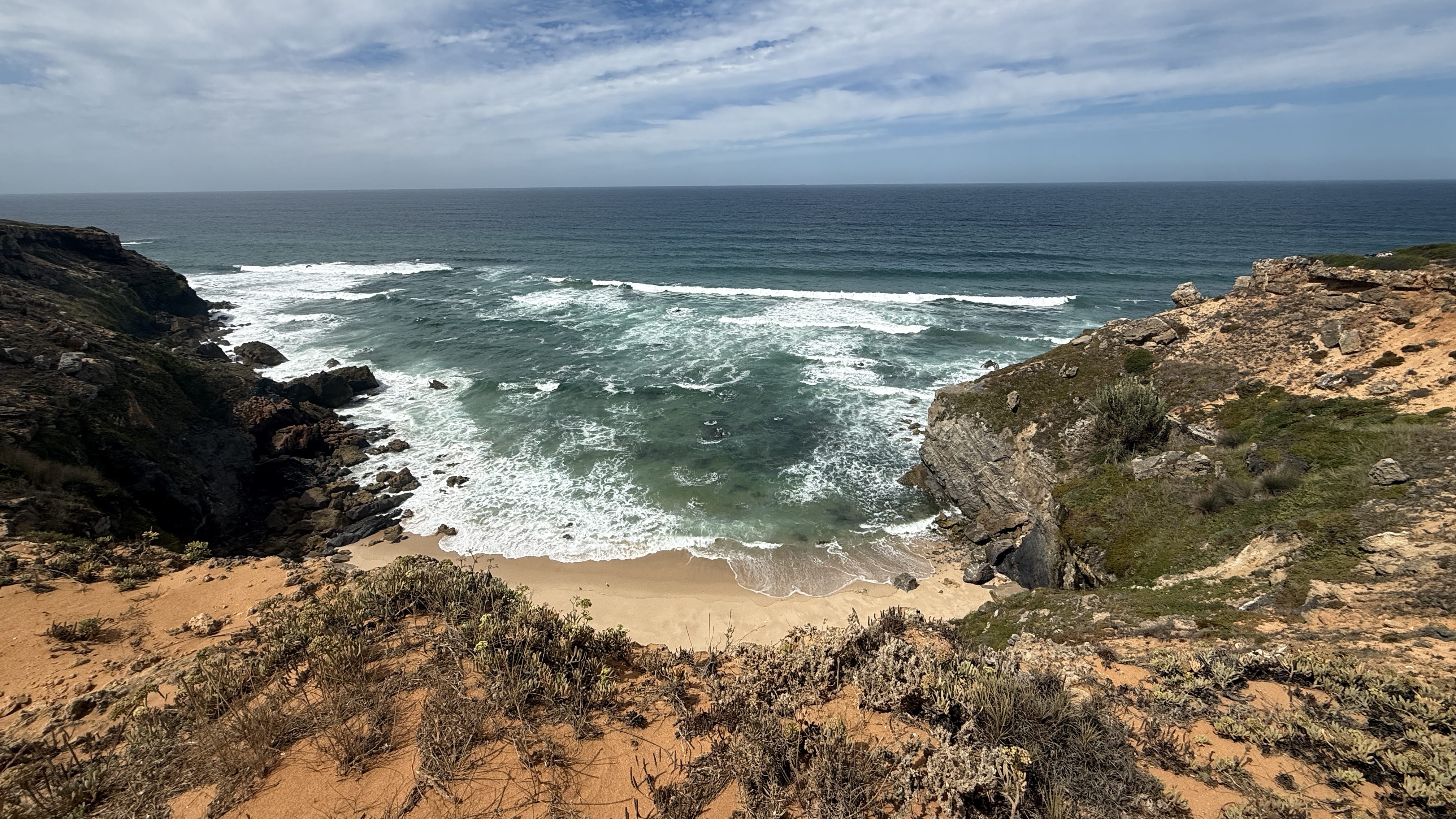 Rocky cliffs with waves crashing below and a hidden beach tucked between the rocks on Portugal’s Fisherman’s Trail.