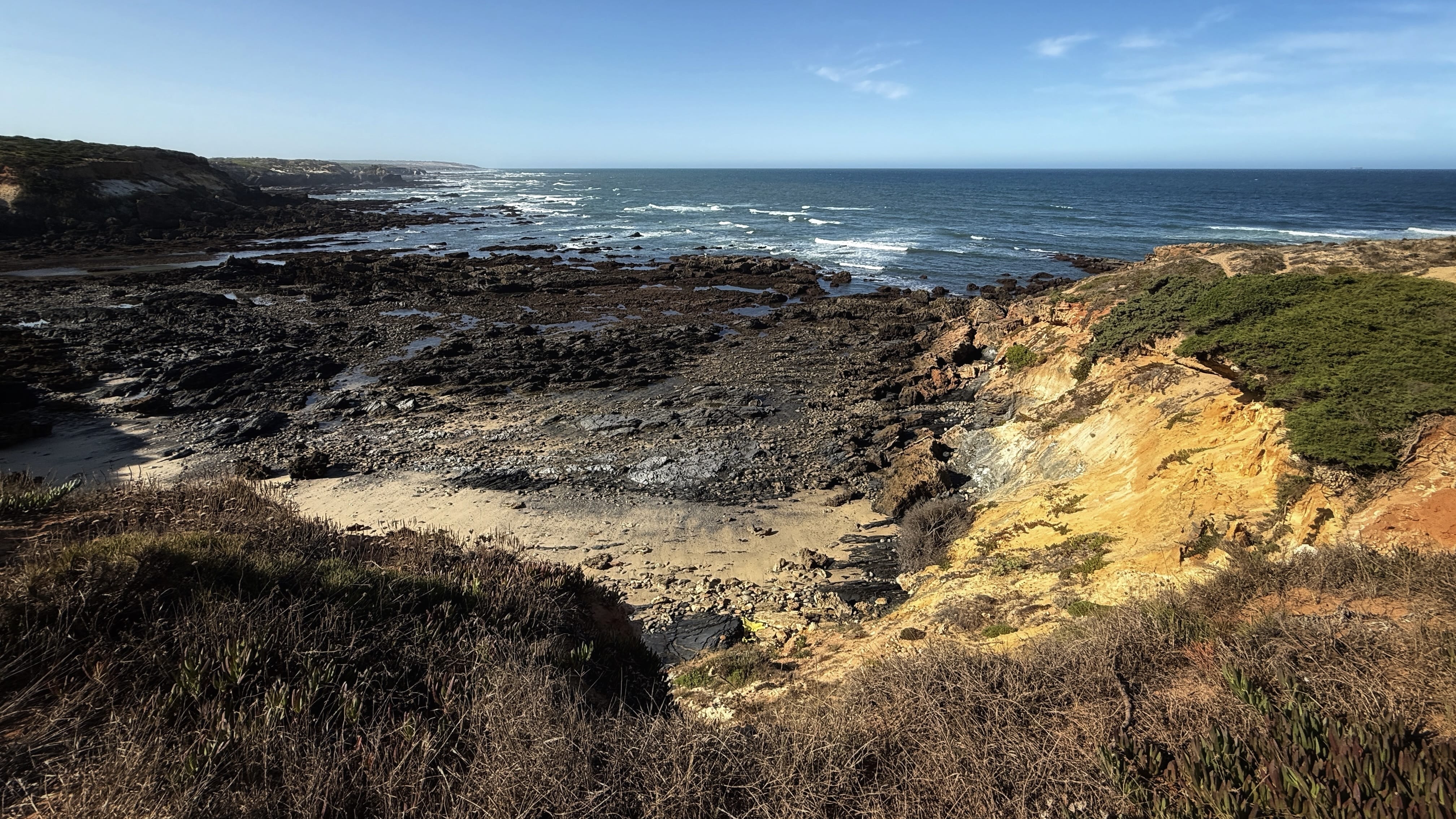 Golden-yellow cliffs and dark rocky shoreline along the Fisherman’s Trail between Vila Nova de Milfontes and Almograve, Portugal.