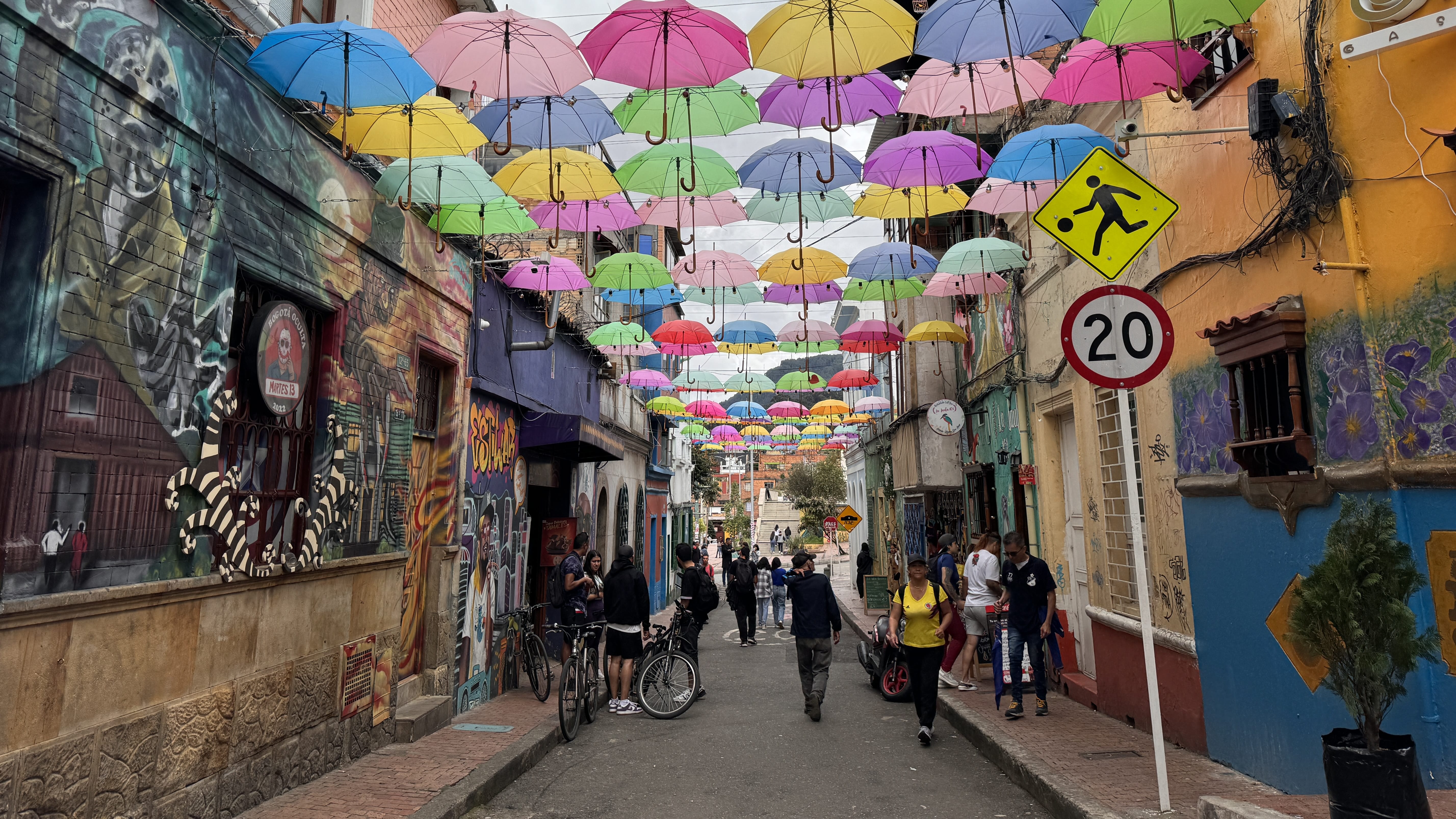 Close-up view of Bogotá’s umbrella street in La Candelaria, with pastel umbrellas suspended above murals and pedestrians, seen during 2 days in Bogotá.