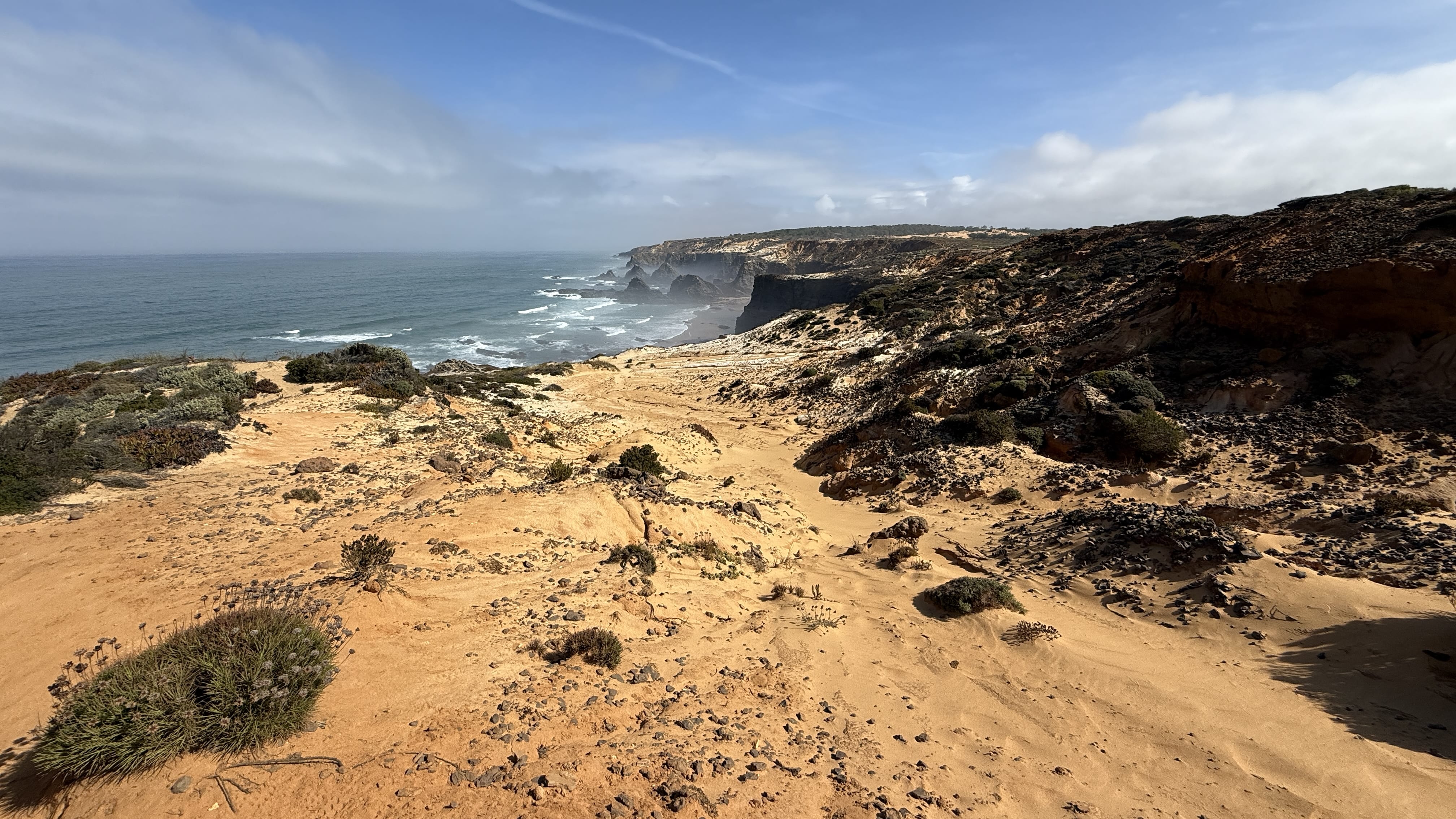 Panorama of terraced cliffs and hidden beaches along the Alentejo coastline near Zambujeira do Mar.