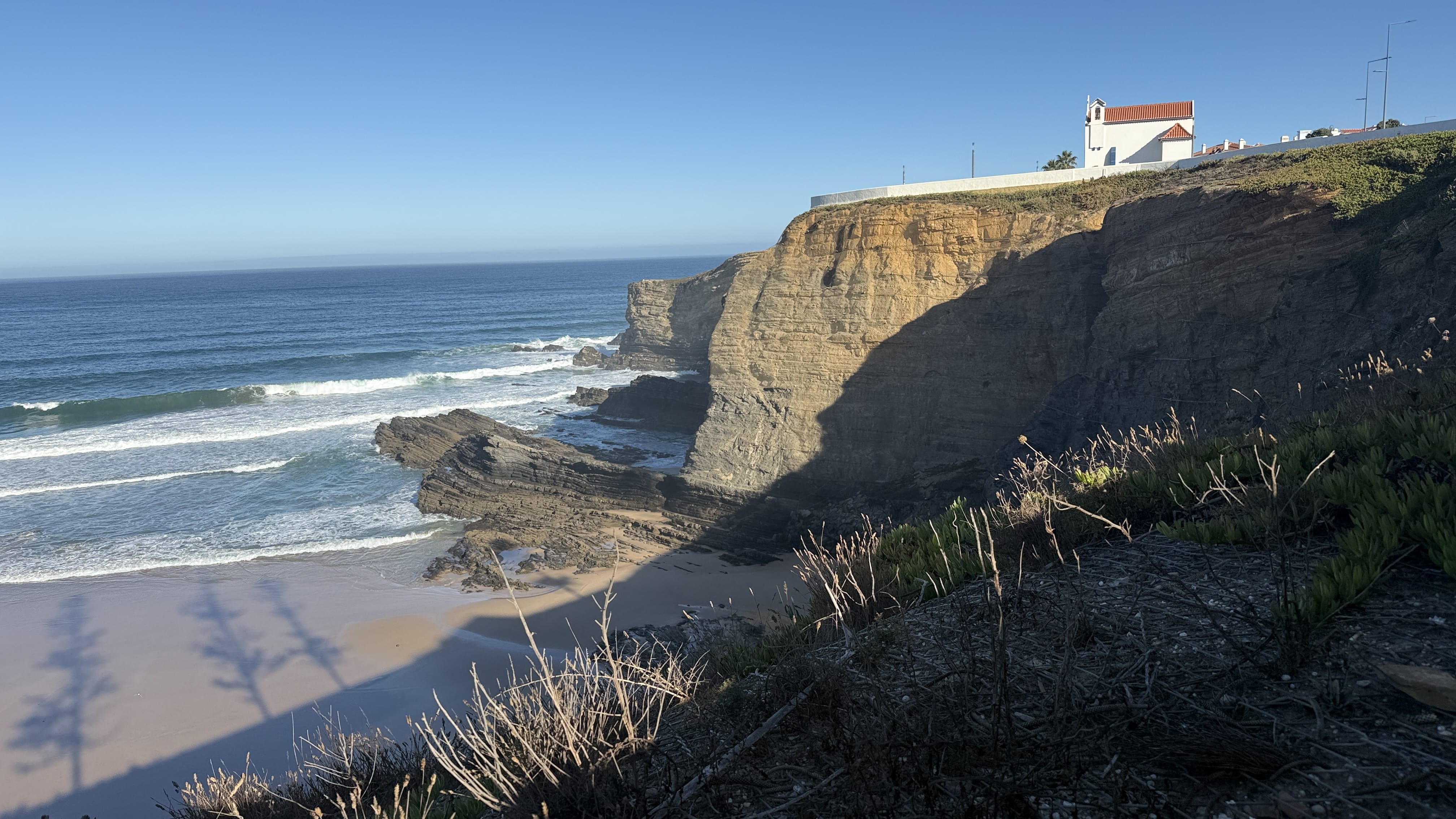 Whitewashed chapel overlooking dramatic sandstone cliffs and the Atlantic Ocean in Zambujeira do Mar, Portugal.