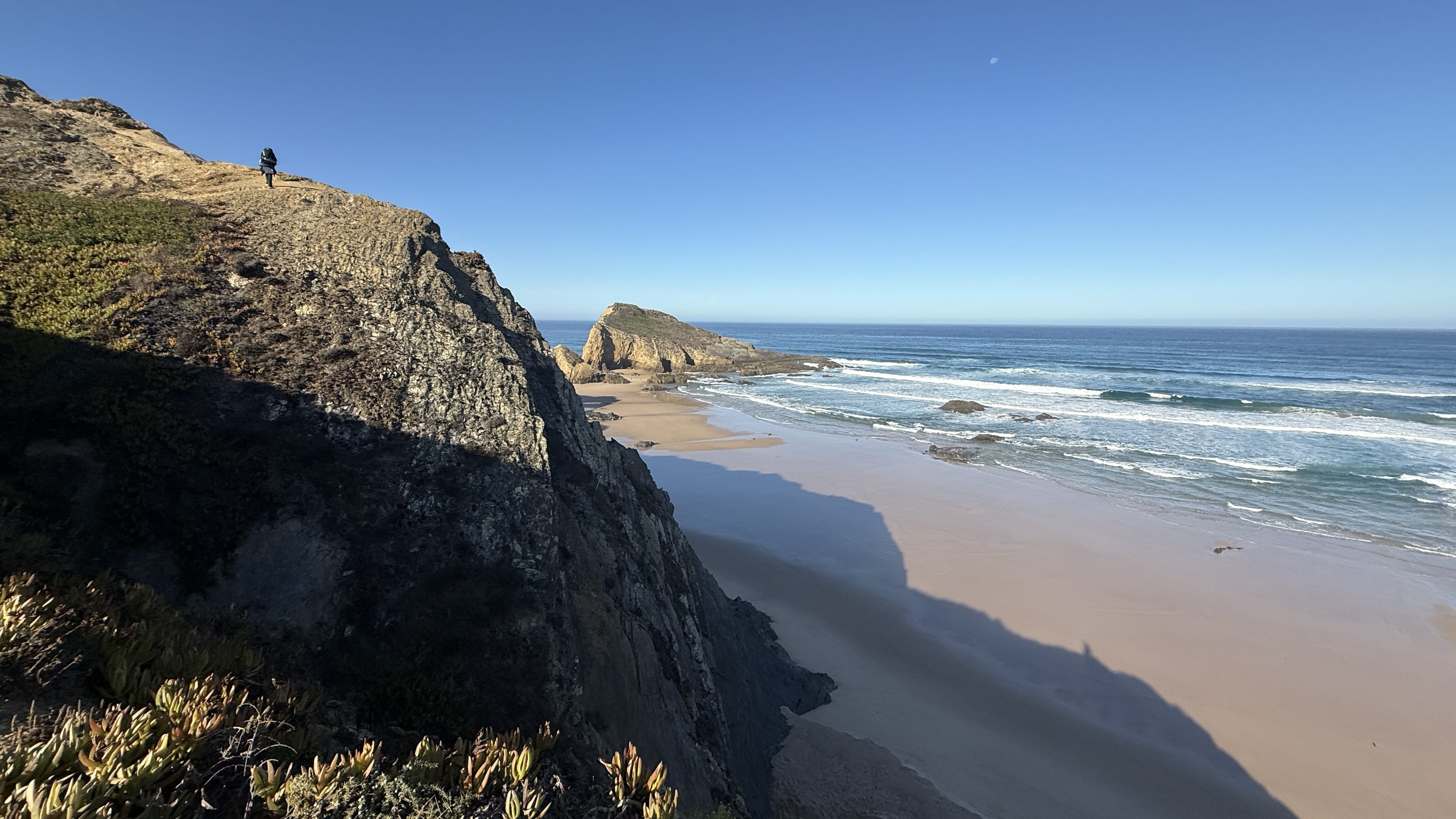 Hiker climbing a steep cliffside trail above the beach on the Fishermen’s Trail, Portugal.