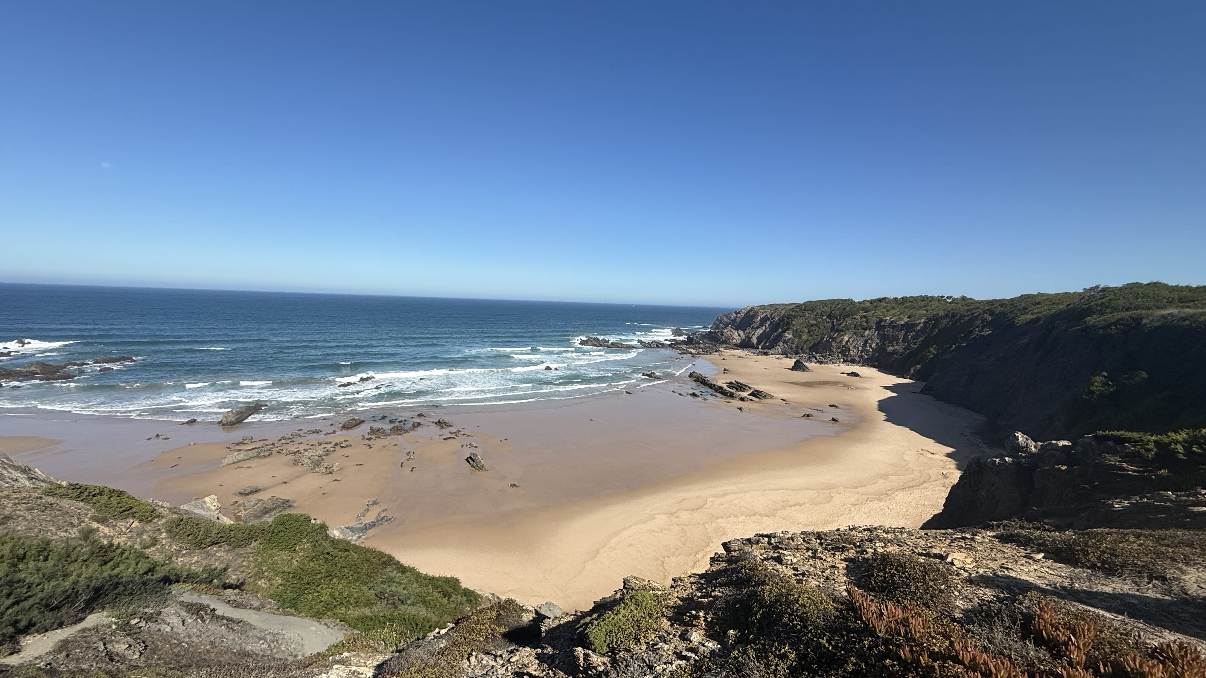 Expansive sandy beach framed by rugged cliffs and Atlantic waves on the Fishermen’s Trail, Portugal.