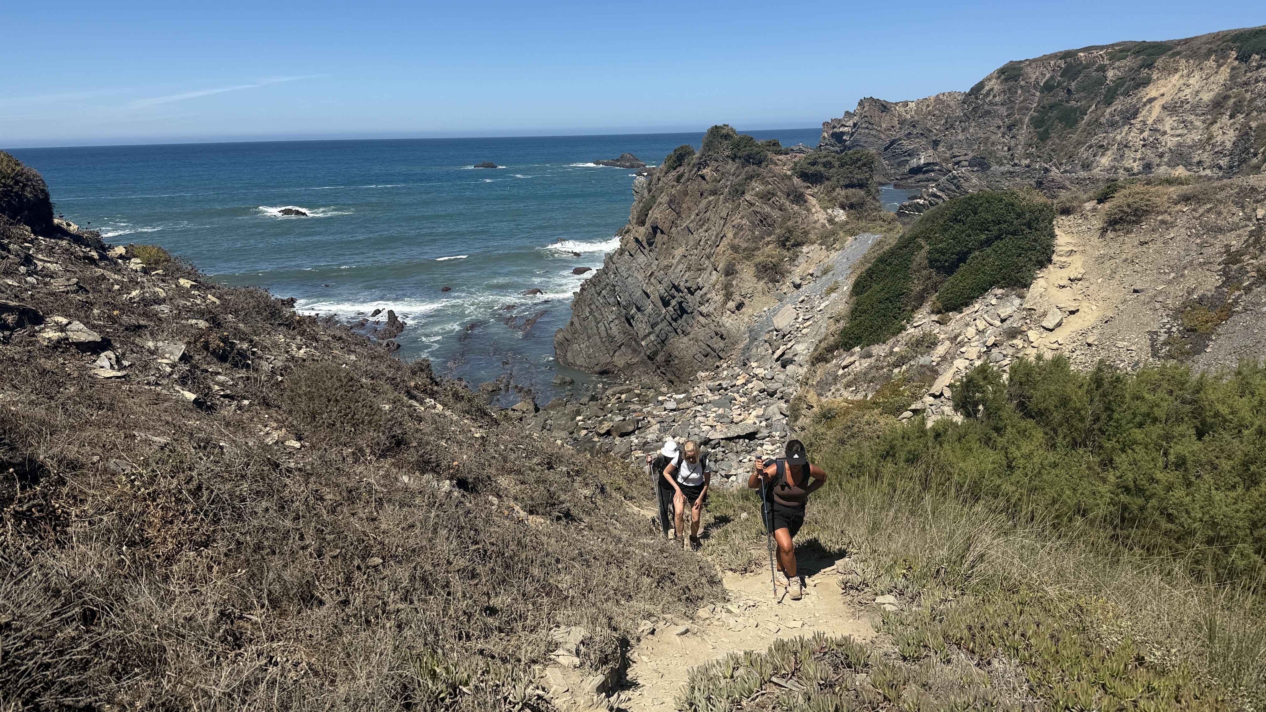 Group of hikers climbing a steep rocky path with the Atlantic Ocean in the background, Fisherman’s Trail, Portugal.