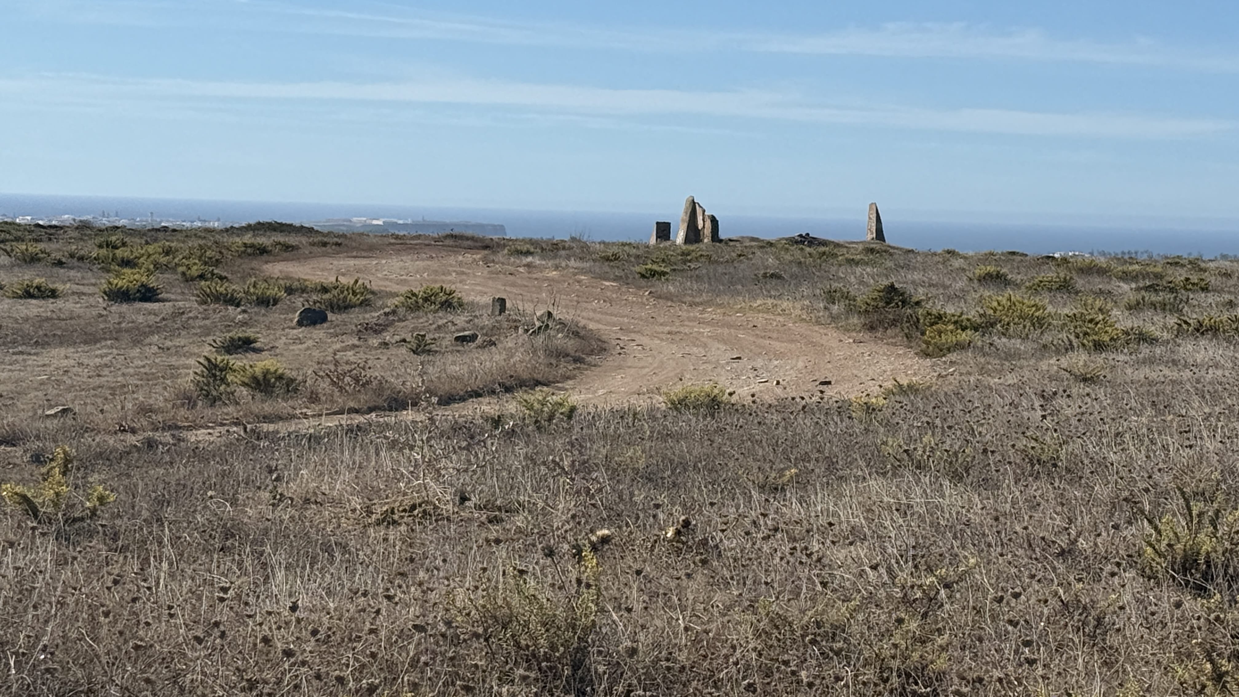 Cluster of megalithic standing stones on the horizon with ocean views in the background near Sagres, Portugal.