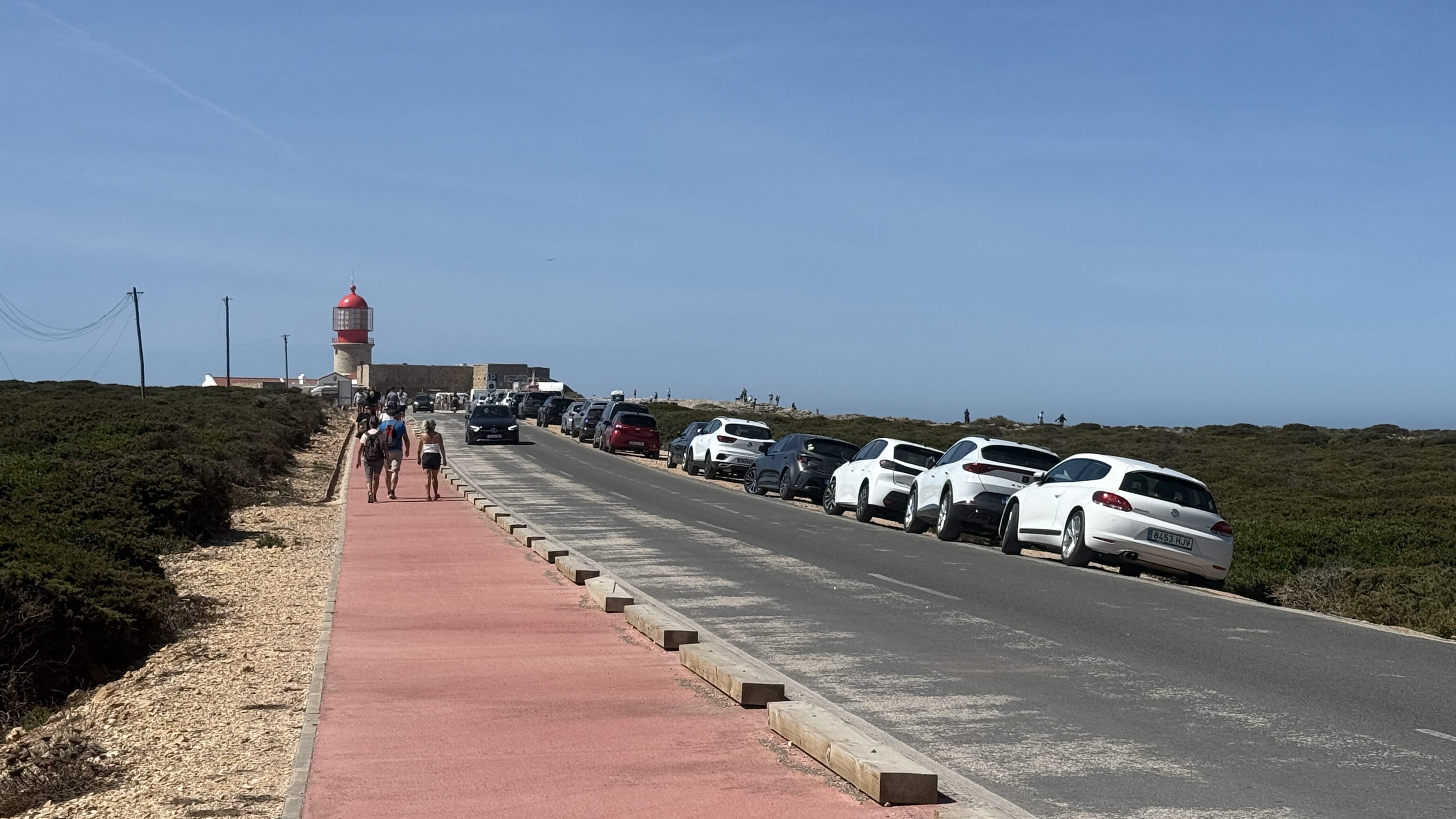Road and walkway leading to Cabo de São Vicente lighthouse in Sagres, Portugal, with tourists approaching.