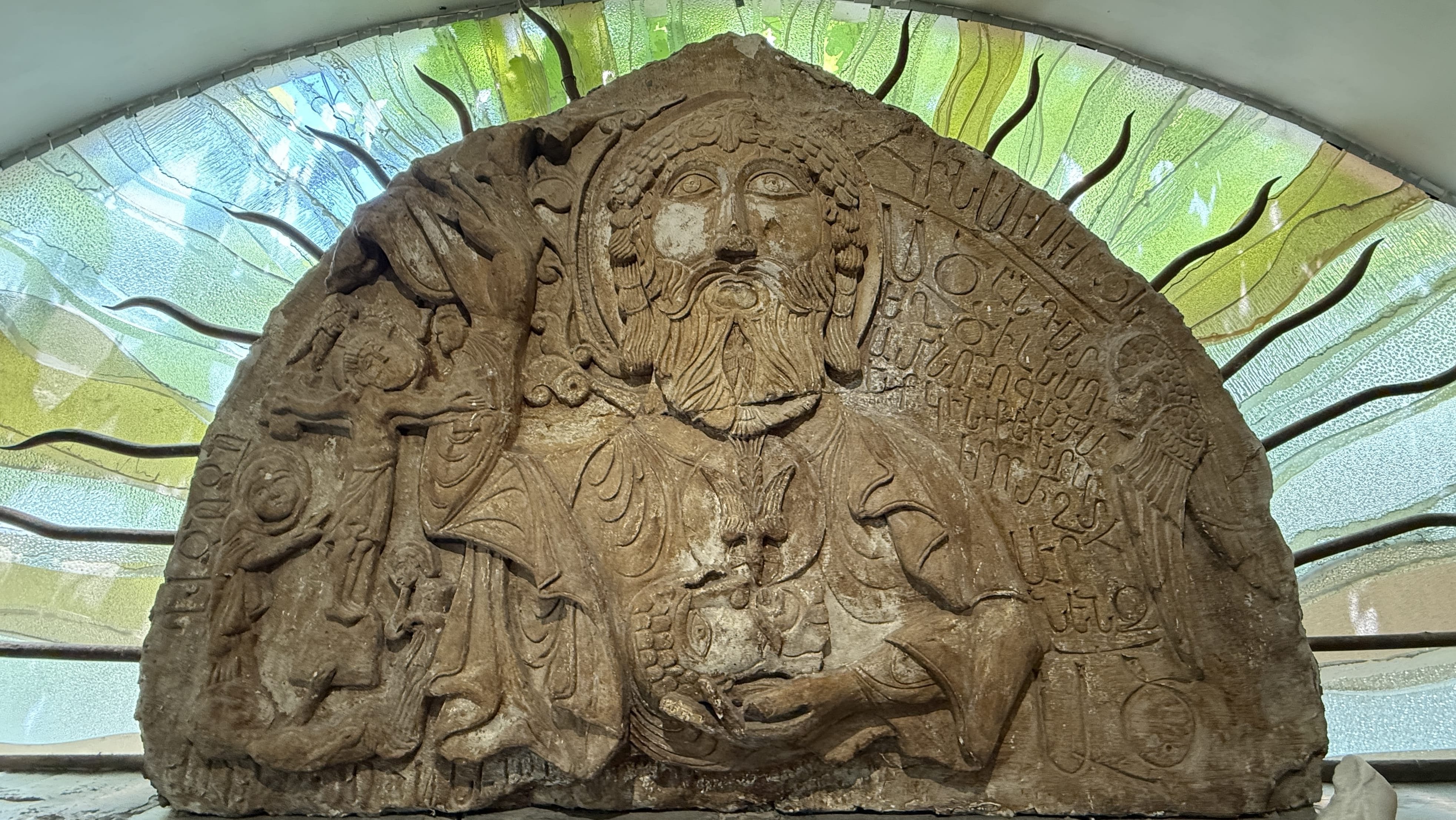 Ancient stone relief of Christ with Armenian inscriptions, displayed with stained glass backdrop at Lusik Aguletsi House Museum – 7 Days in Armenia.