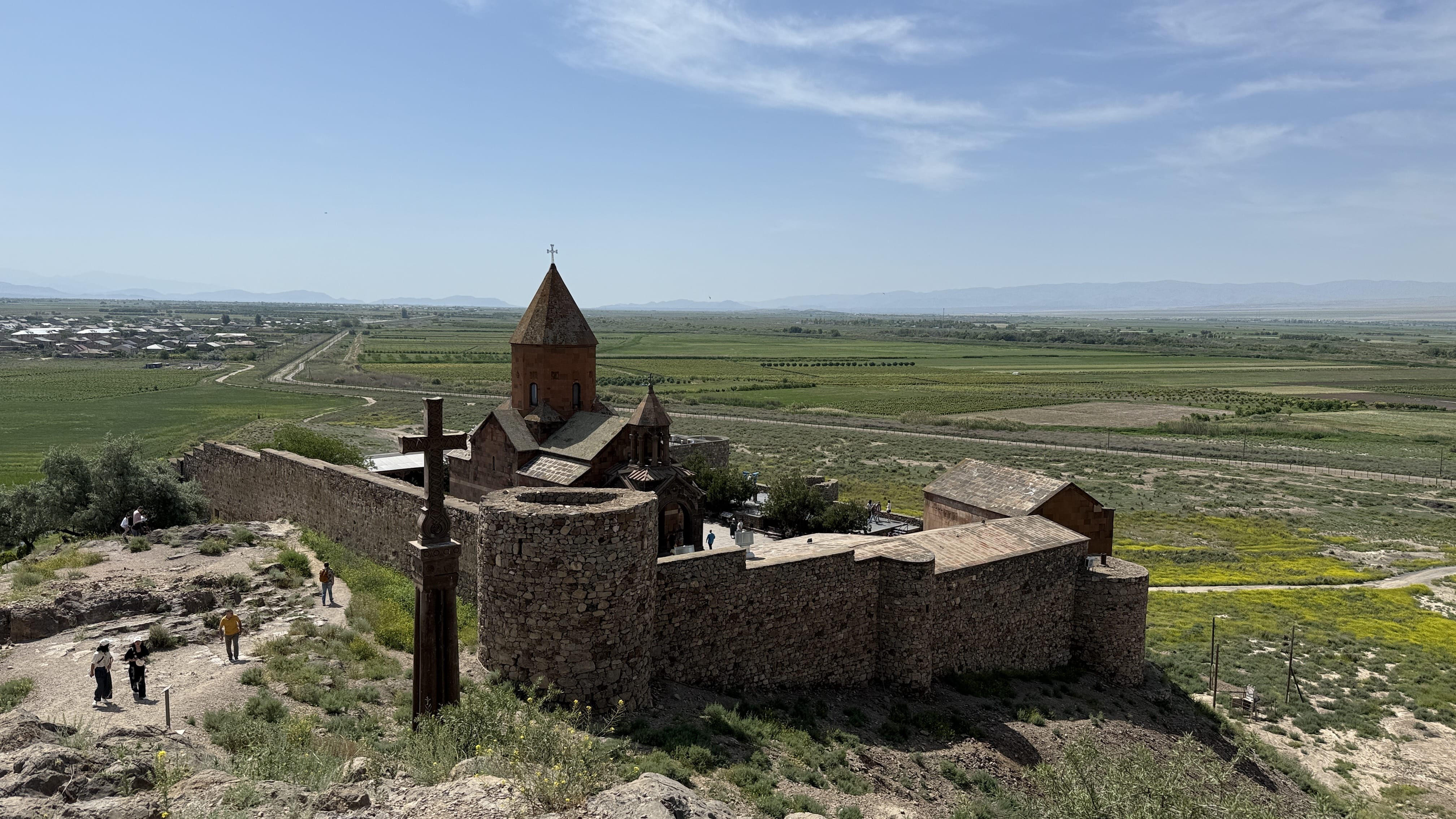 Stone-walled Khor Virap Monastery in Armenia, overlooking green fields and villages on the Ararat Plain.