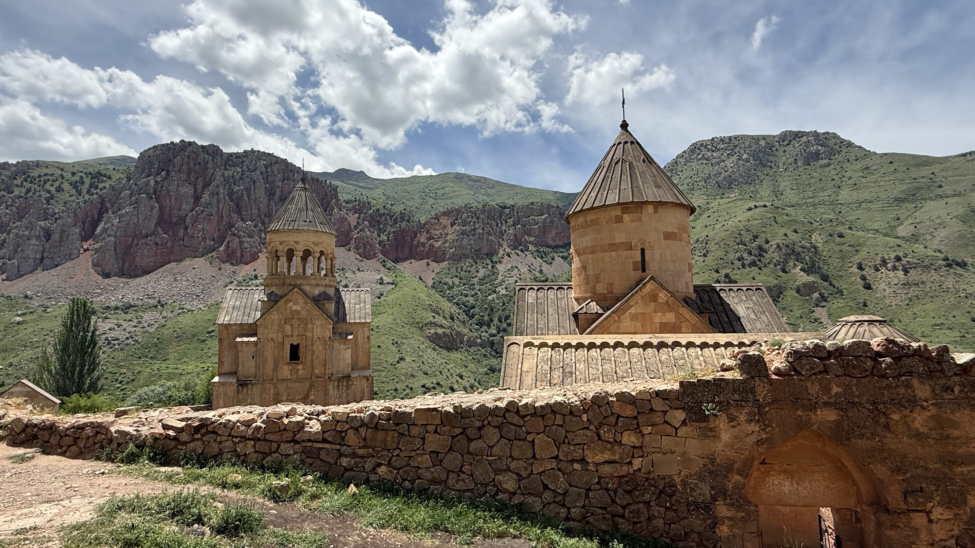 : Noravank Monastery churches surrounded by green hills and rocky cliffs.