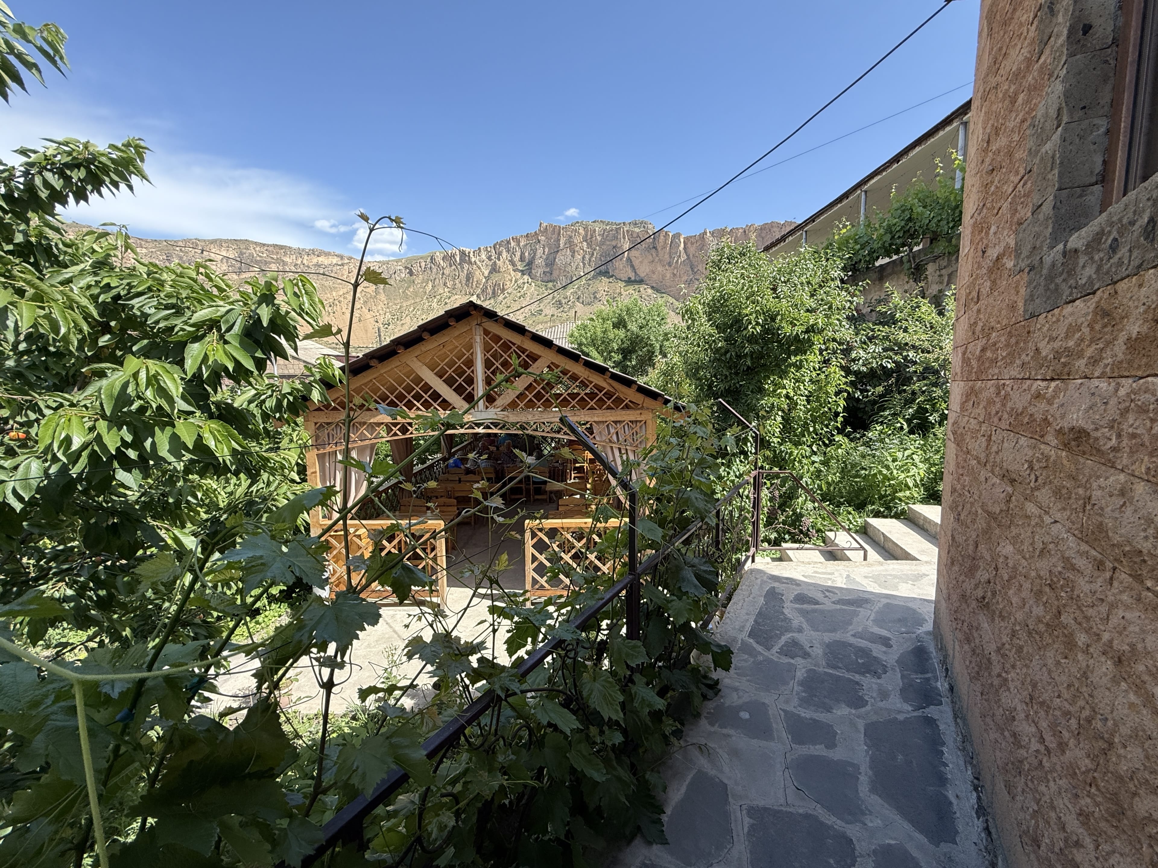 Outdoor wooden gazebo surrounded by grapevines and greenery at a guesthouse in Armenia.