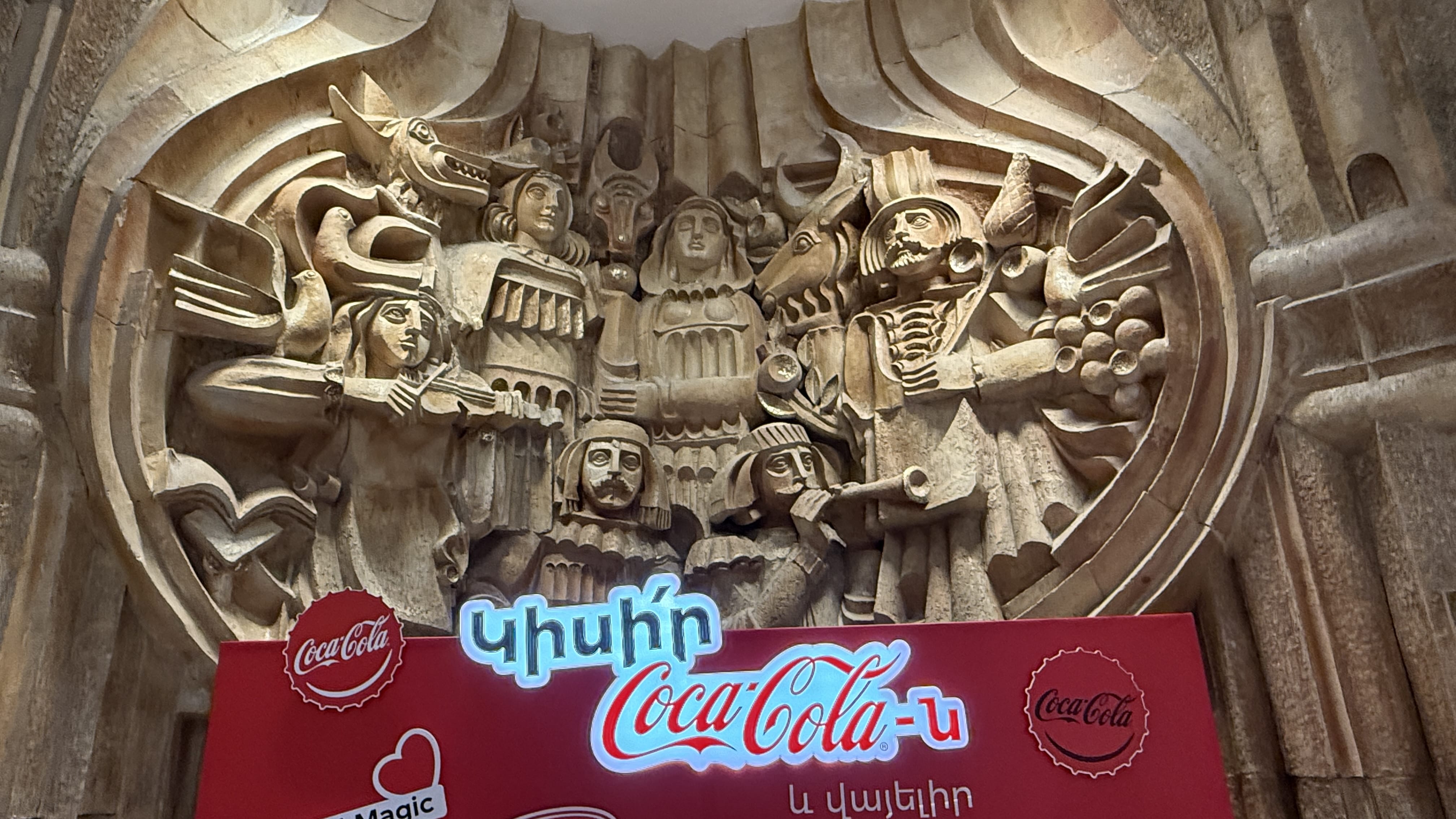 Soviet-era bas-relief sculpture inside Yerevan’s Russian Theater, partly covered by a Coca-Cola sign – 24 Hours in Yerevan.