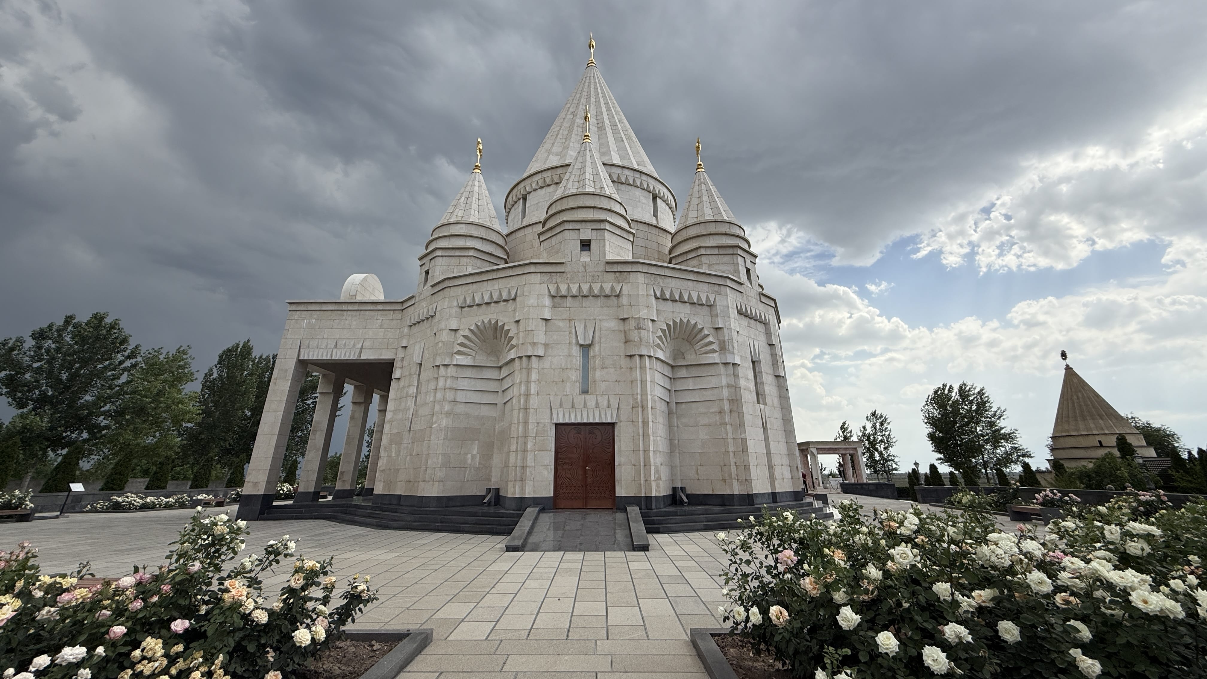 Exterior view of Aknalich Yazidi Temple in Armenia with rose gardens and storm clouds in the sky, photographed during seven days in Armenia.