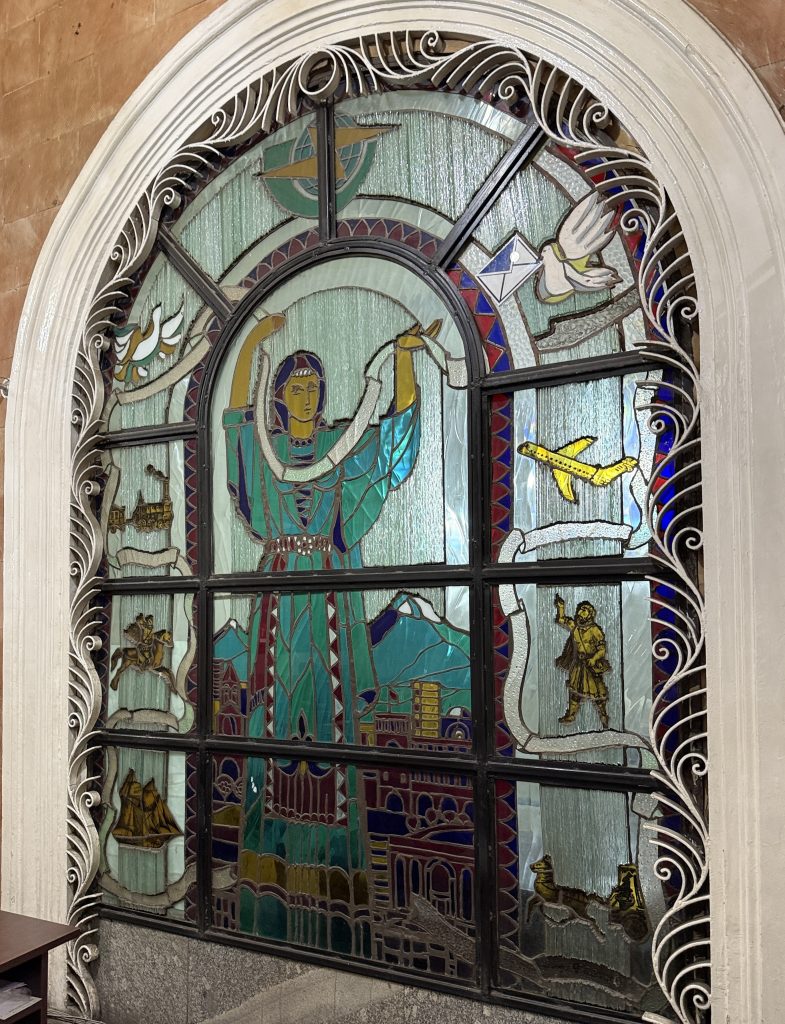 Soviet-era stained glass window inside the Yerevan post office, showing a woman holding a scroll, doves, an airplane, and symbolic Armenian scenes – 24 Hours in Yerevan.