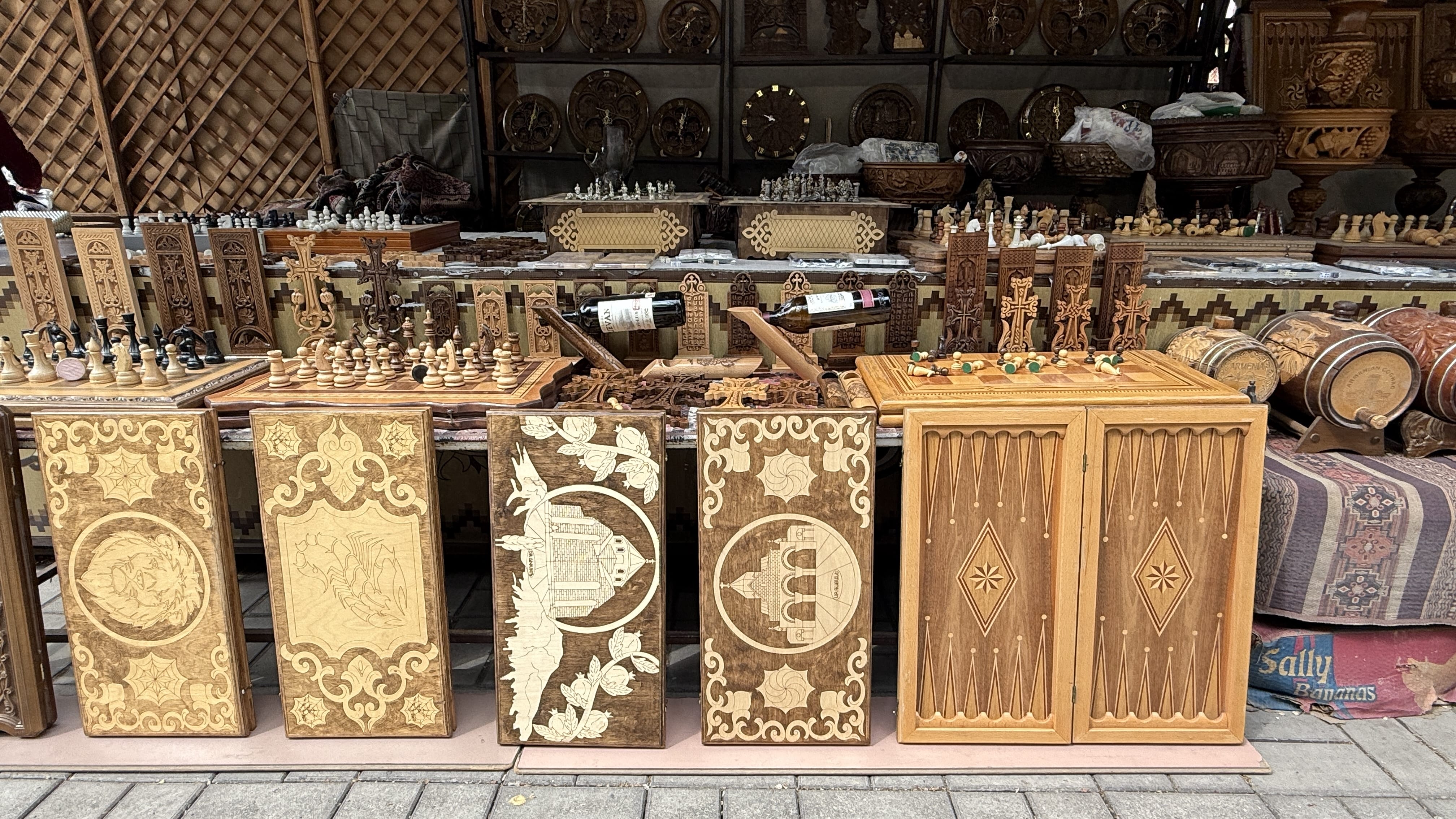 Wooden chess boards, backgammon sets, and khachkar-style carvings displayed for sale at Vernissage Market in Yerevan, Armenia.