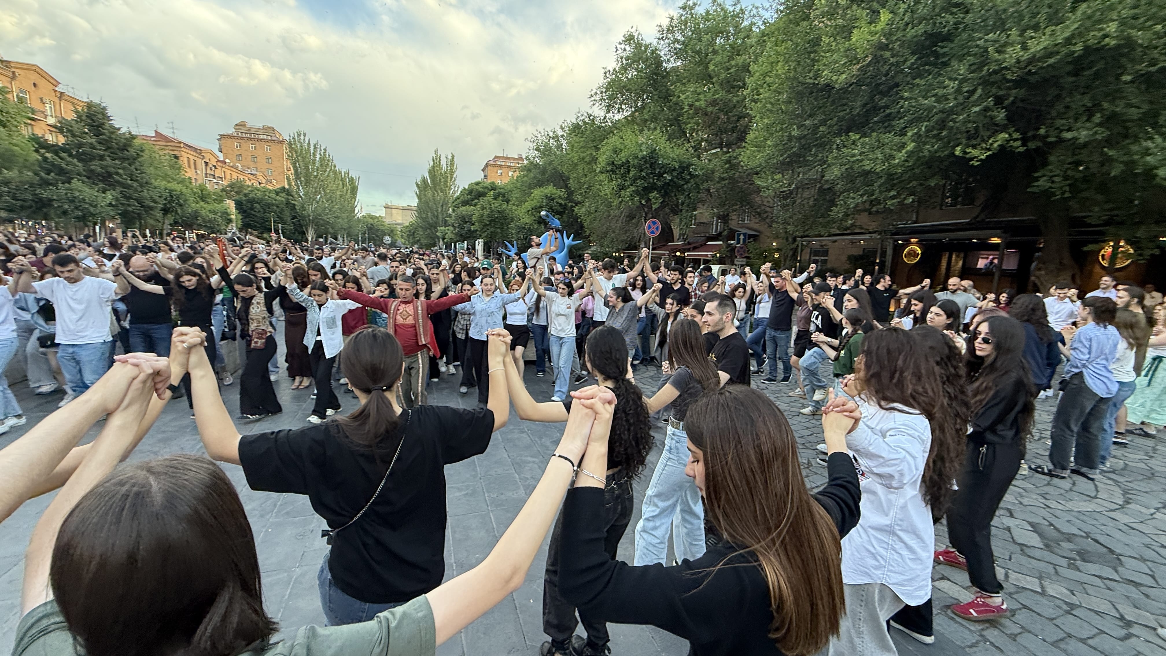 Large crowd holding hands in a circle while performing traditional Armenian dance in an outdoor square in Yerevan.