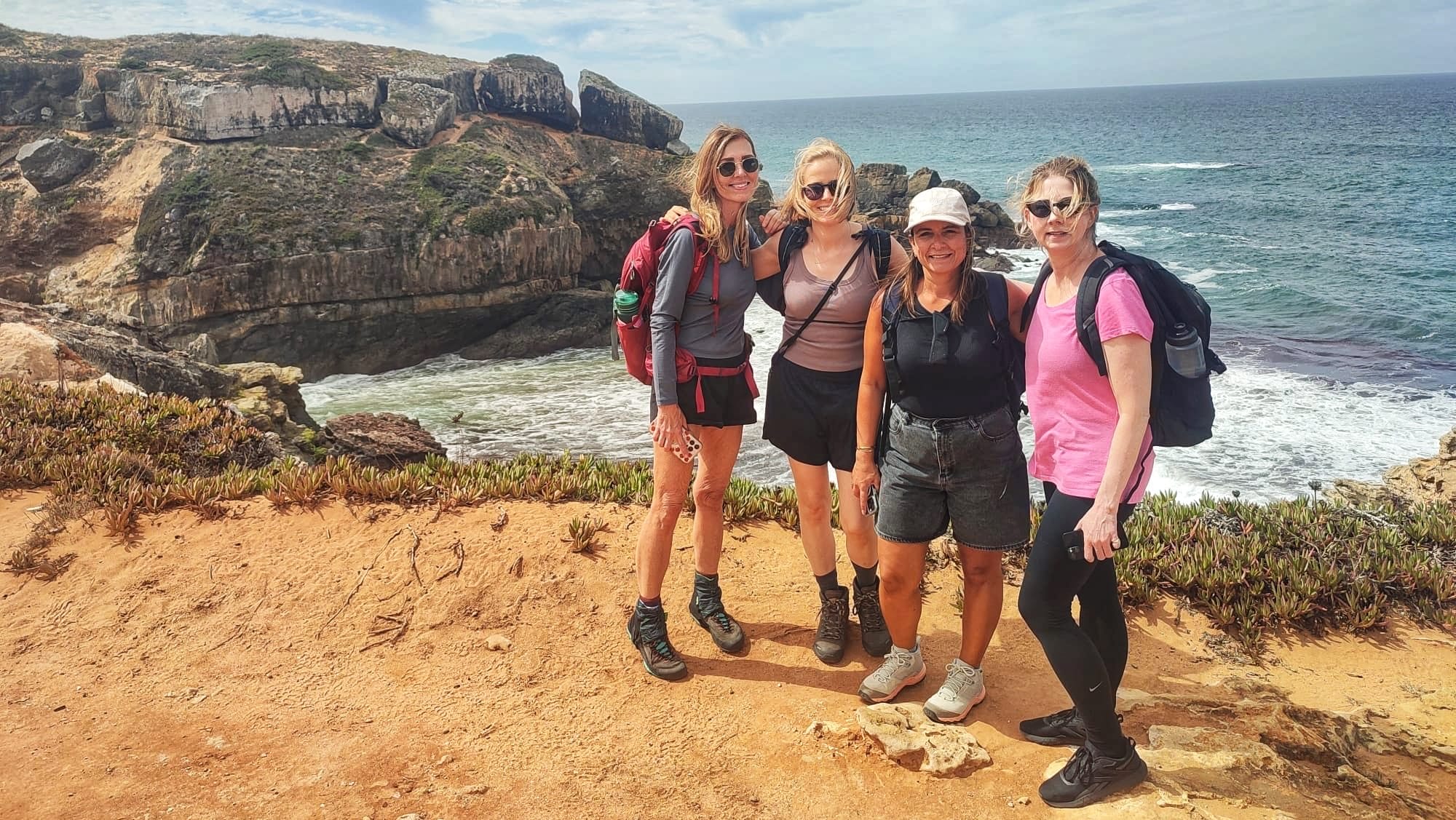 Four women hikers on Portugal’s Fisherman’s Trail near Malhão, standing on coastal cliffs above the Atlantic Ocean.
