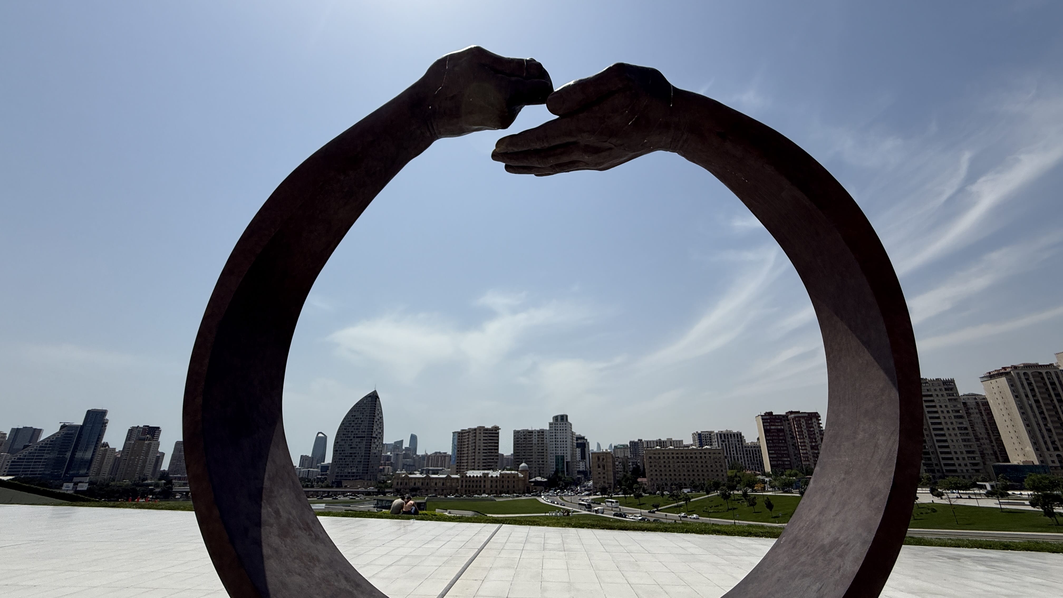 Bronze sculpture of two hands forming a circular shape with the Baku skyline in the background — 2 Days in Baku sculpture park.