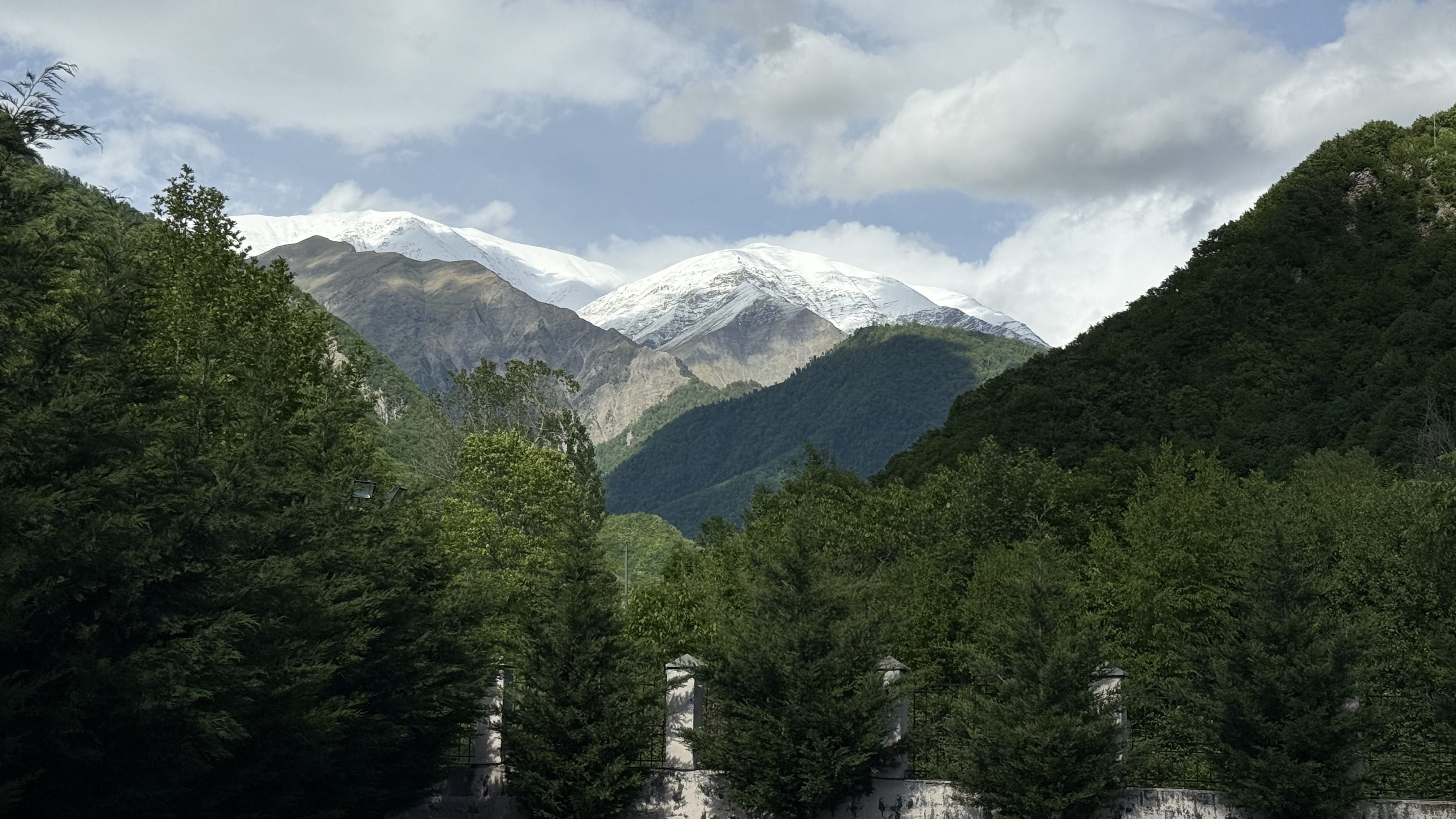 Snow-capped peaks of the Caucasus Mountains framed by green forested hills near Kish, photographed during my 7 Days in Azerbaijan trip.
