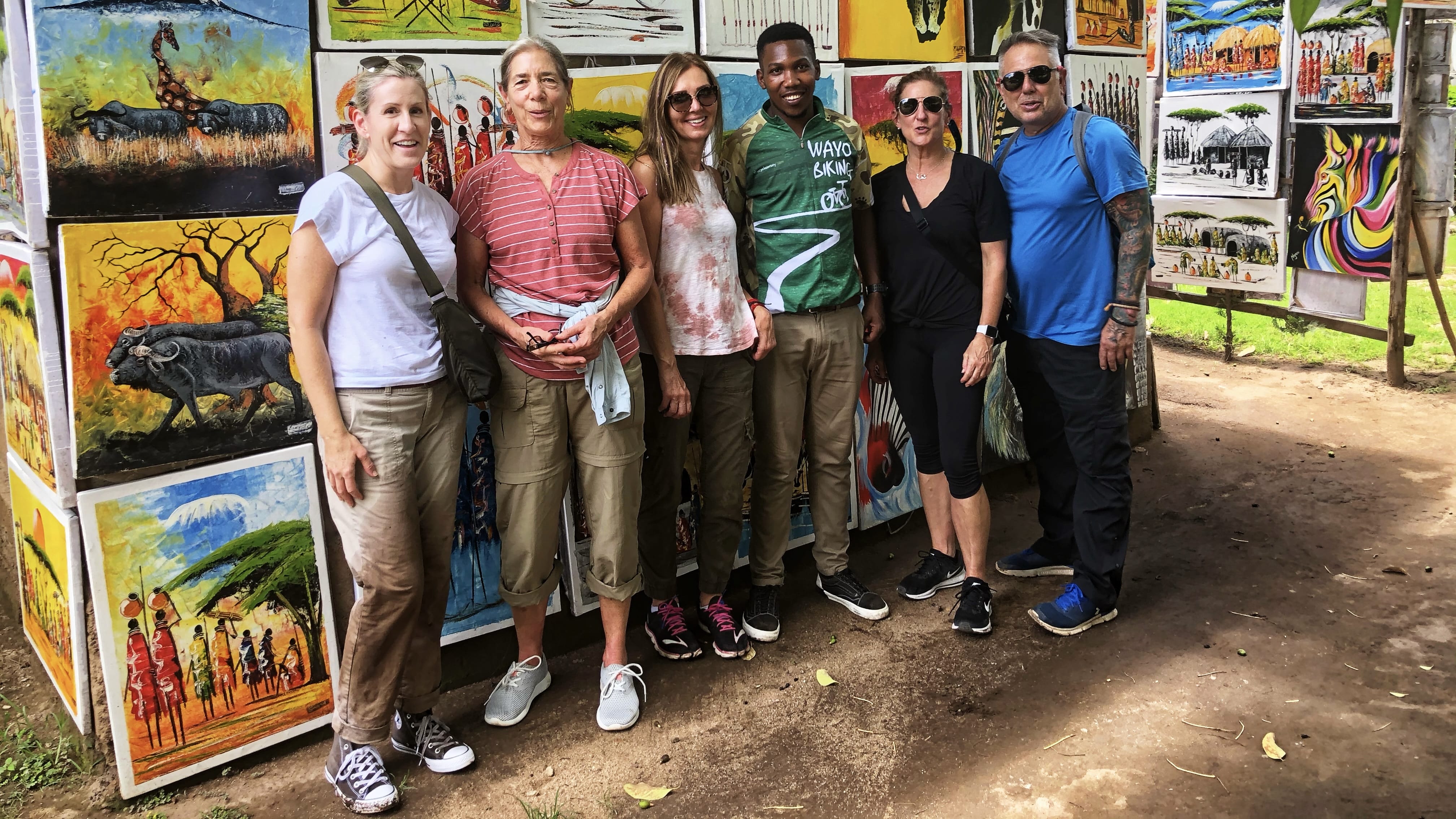 Group standing in front of colorful wildlife paintings at a local art stall in Mto wa Mbu, Tanzania, near Lake Manyara