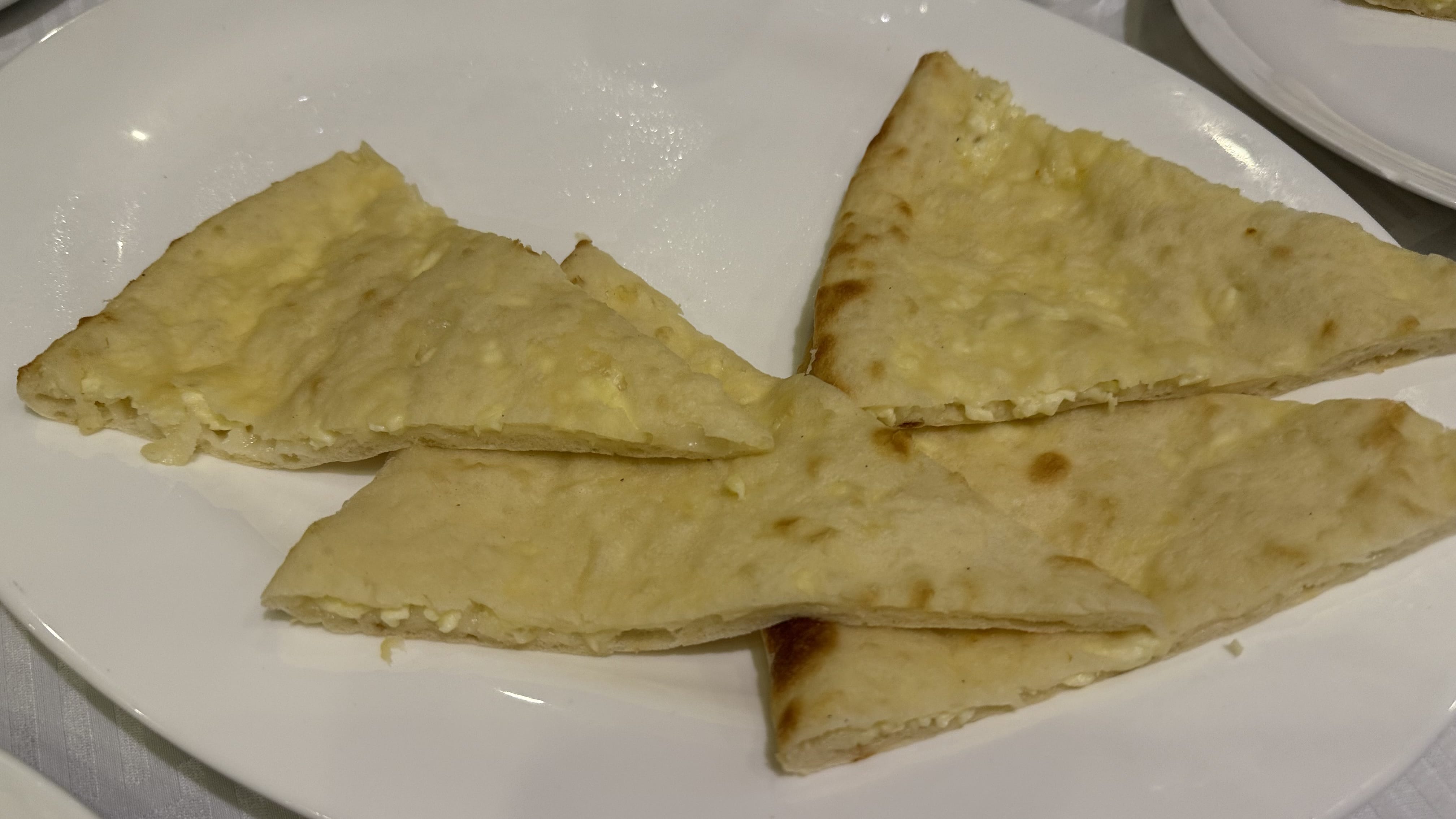 Slices of Imeruli khachapuri, a Georgian cheese-filled flatbread, served on a white plate with melted cheese inside the thin baked dough.