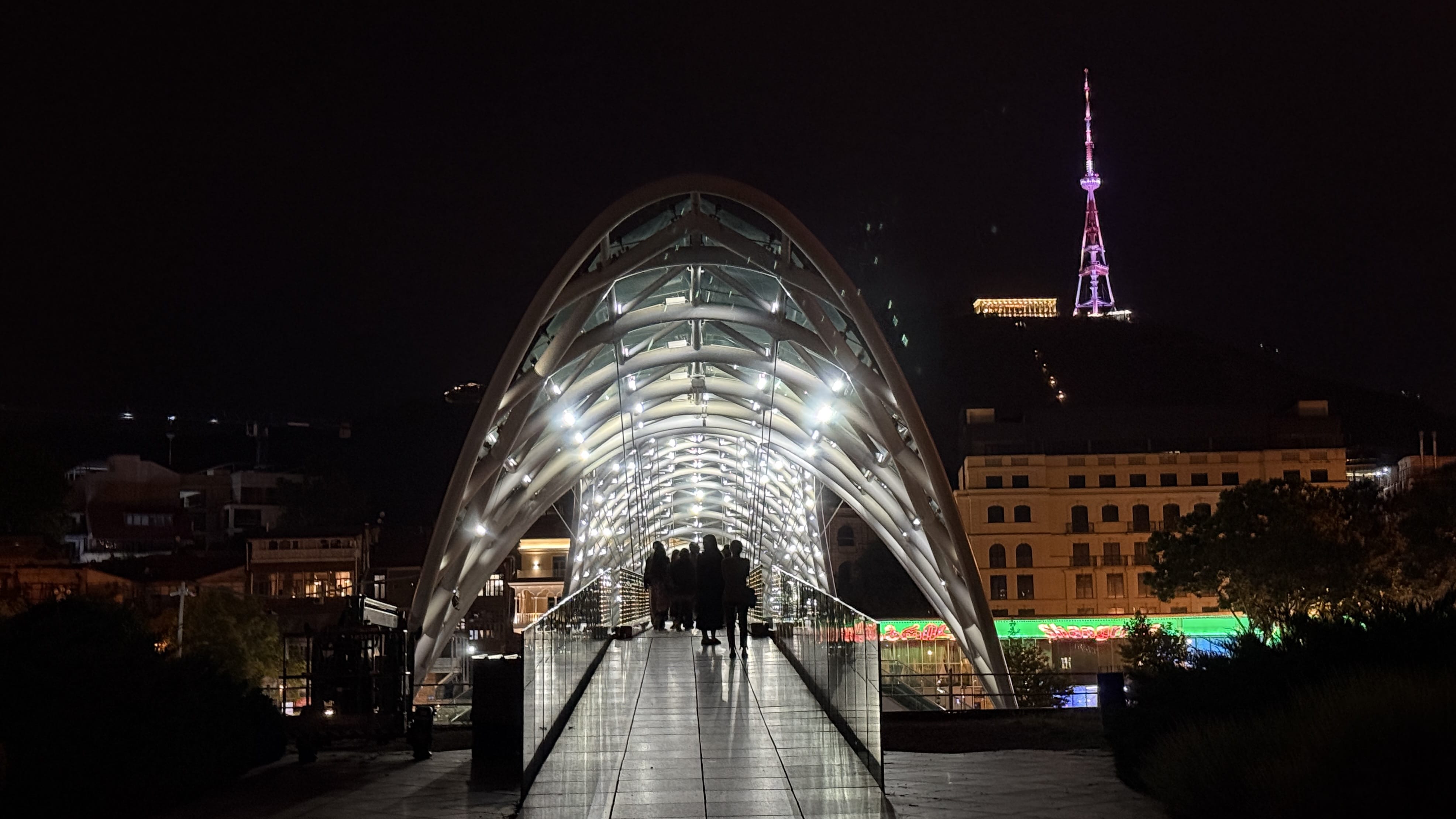 Illuminated Bridge of Peace at night with people walking across in Tbilisi, Georgia