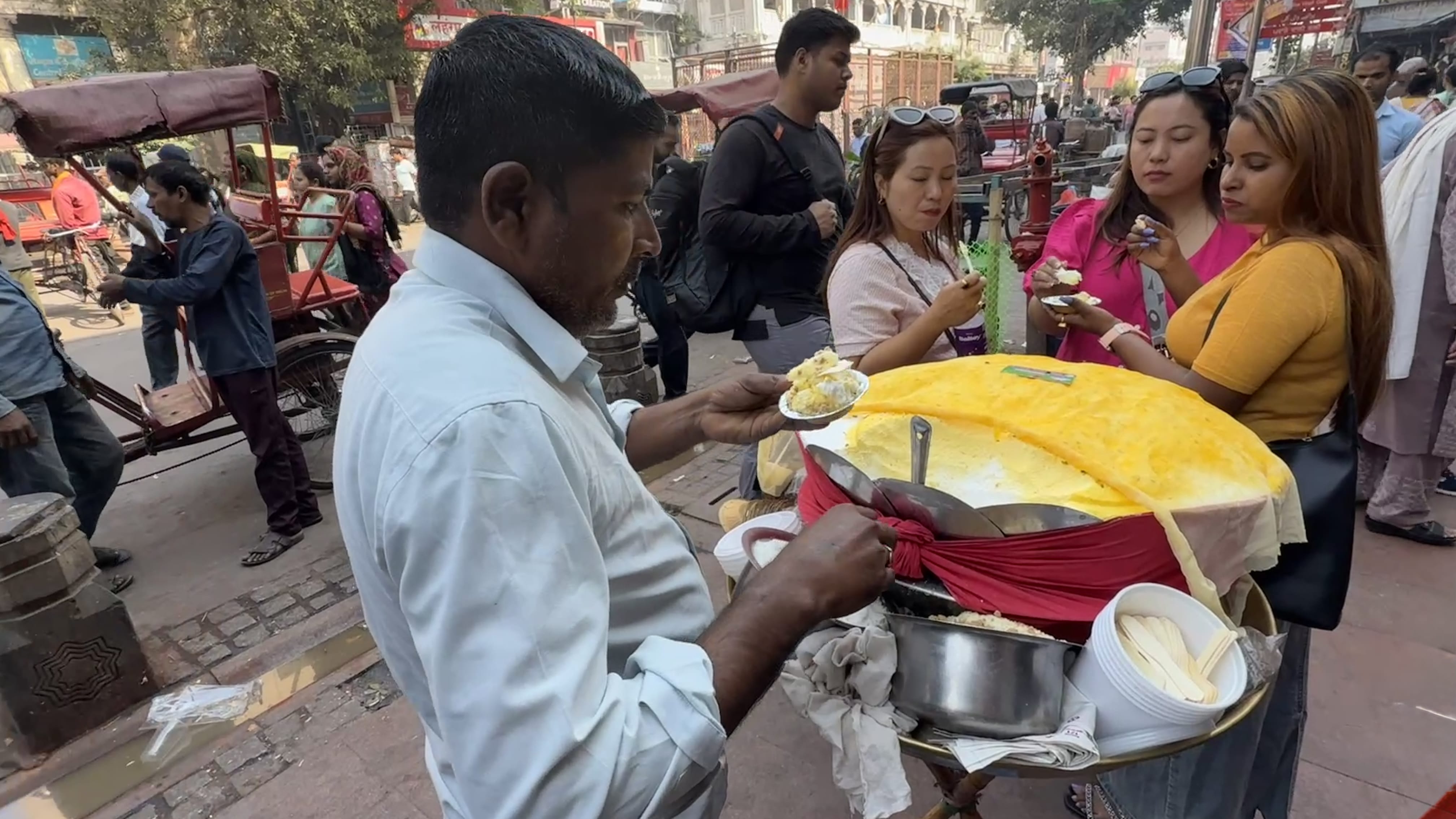 Man serving daulat ki chaat from a street cart in Old Delhi during my 2 Days in Delhi itinerary, with people sampling the dessert beside rickshaws and market stalls.