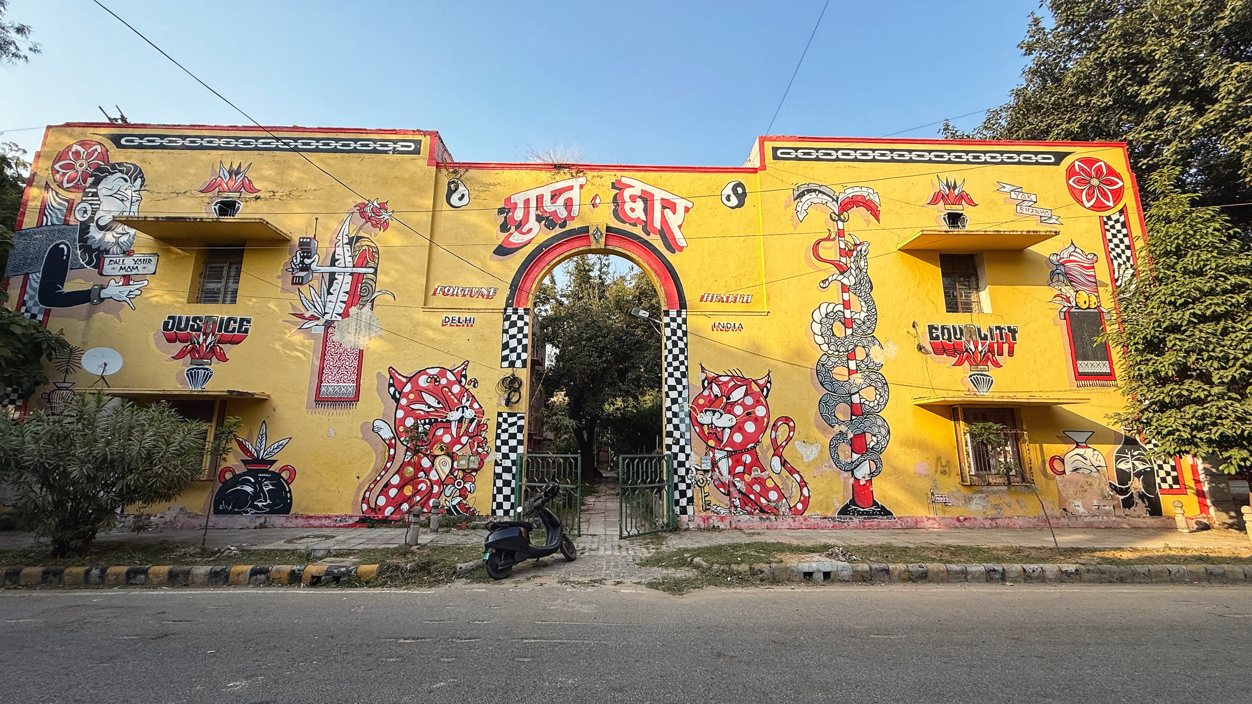 Large yellow mural building in the Lodhi Art District in Delhi, featuring bold street art with red tigers, snakes, graphic lettering, and symbols around a central arched gateway—2 Days in Delhi.