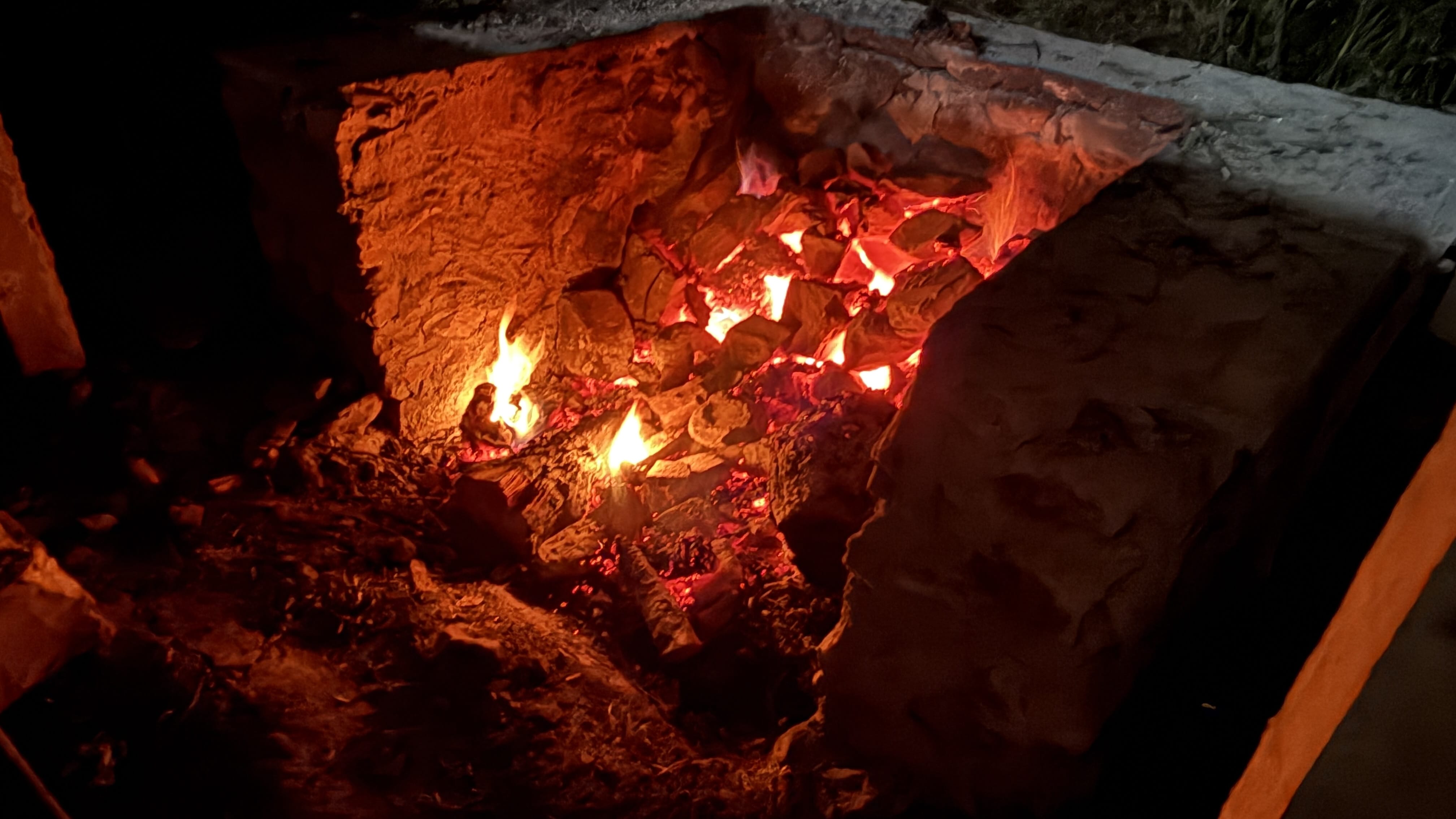 Glowing embers and fire inside a stone pit used to heat river stones for traditional Bhutanese hot stone baths.