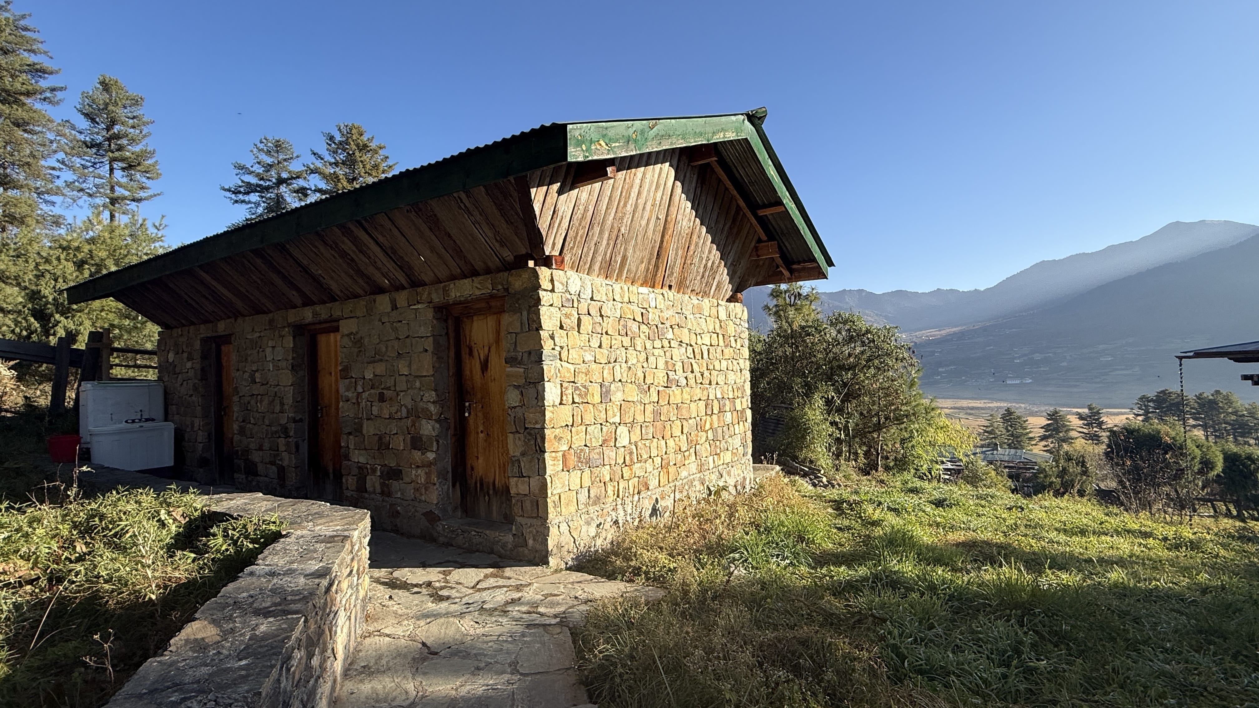 Small stone bathhouse where my hot stone bath would take place in Phobjikha Valley, Bhutan, set on a hillside overlooking fields and distant mountains.