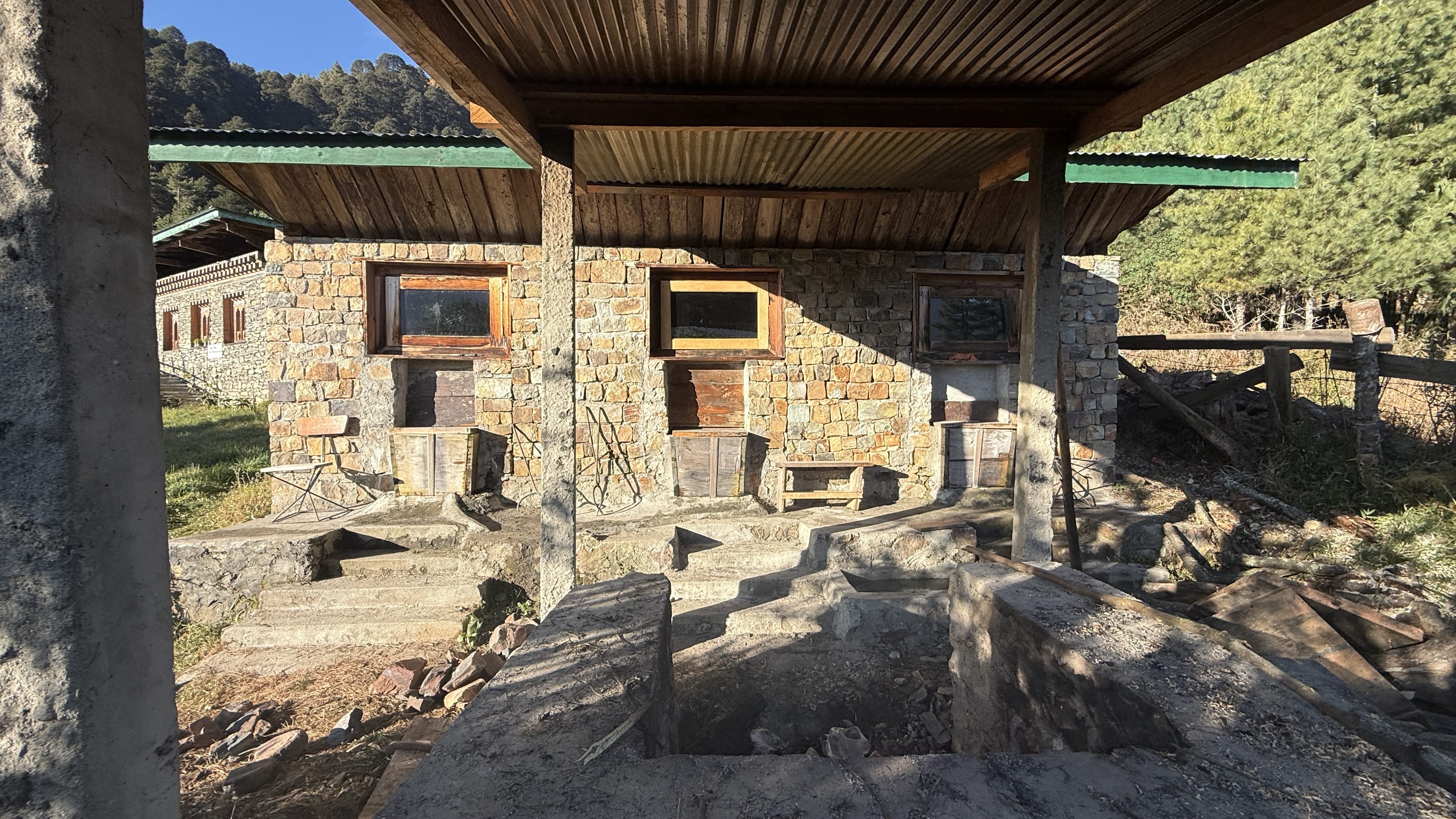 Stone bathhouse wall with long metal tongs used for handling heated river stones in a traditional Bhutanese hot stone bath.