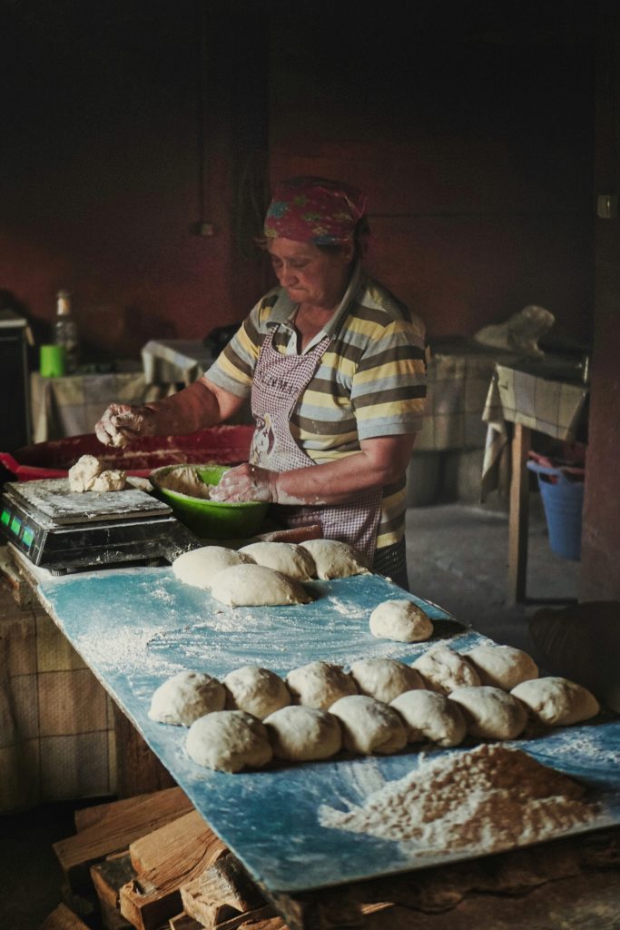 Georgian woman shaping bread dough by hand on a floured table in a traditional kitchen.