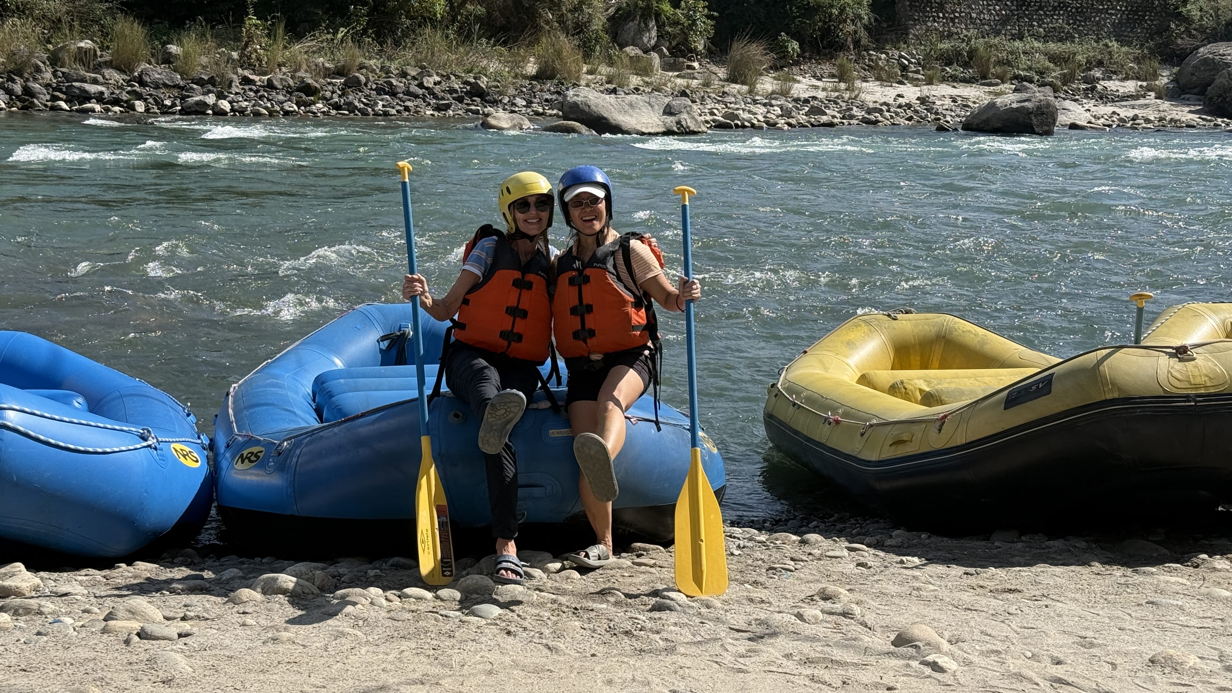 Two travelers in helmets and life vests sitting on rafts along the Mo Chhu River before a rafting trip in Bhutan.