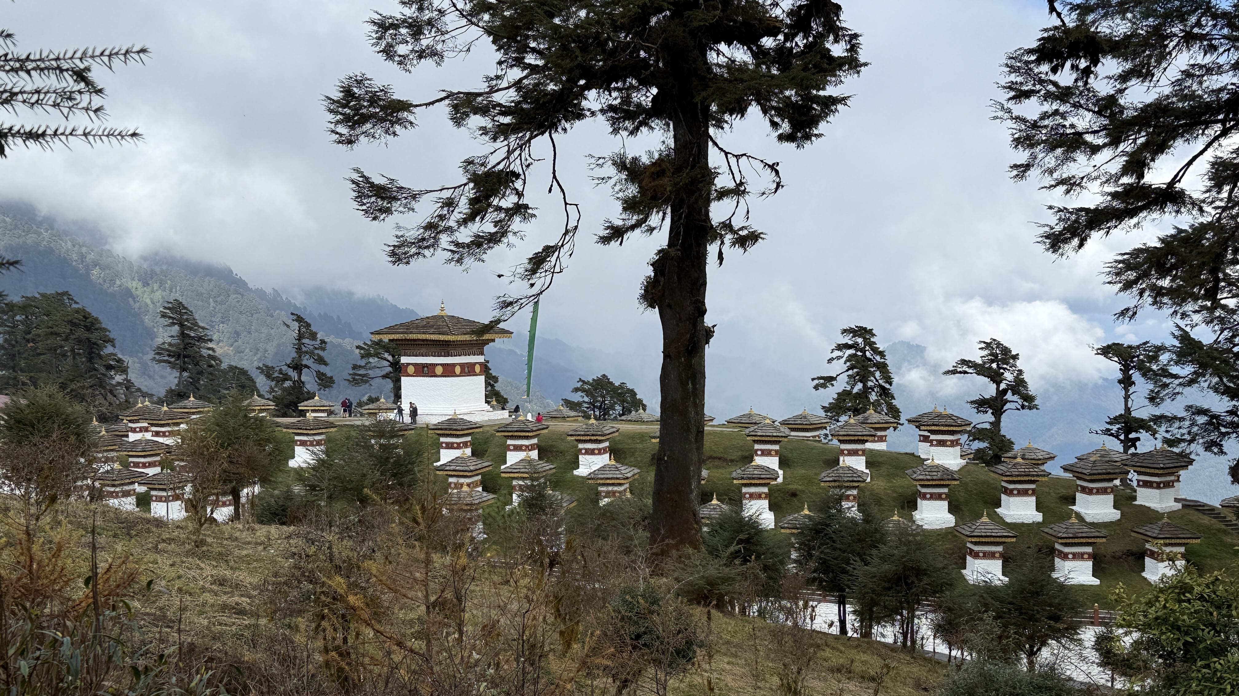 Druk Wangyal Chortens at Dochula Pass in Bhutan, with white stupas on a hillside and misty Himalayan mountains in the background (11 Days in Bhutan)