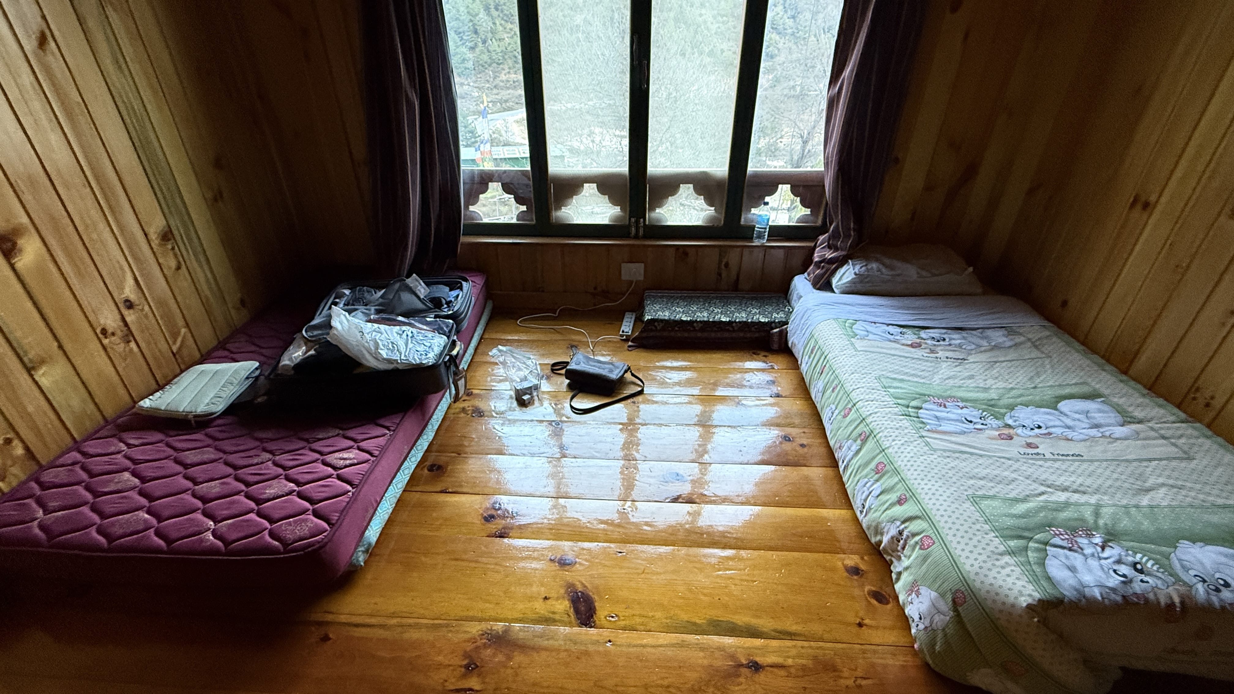 Simple guest room at a traditional Bhutan homestay in Haa Valley, with floor mattresses, wooden walls, and a window overlooking the mountains.