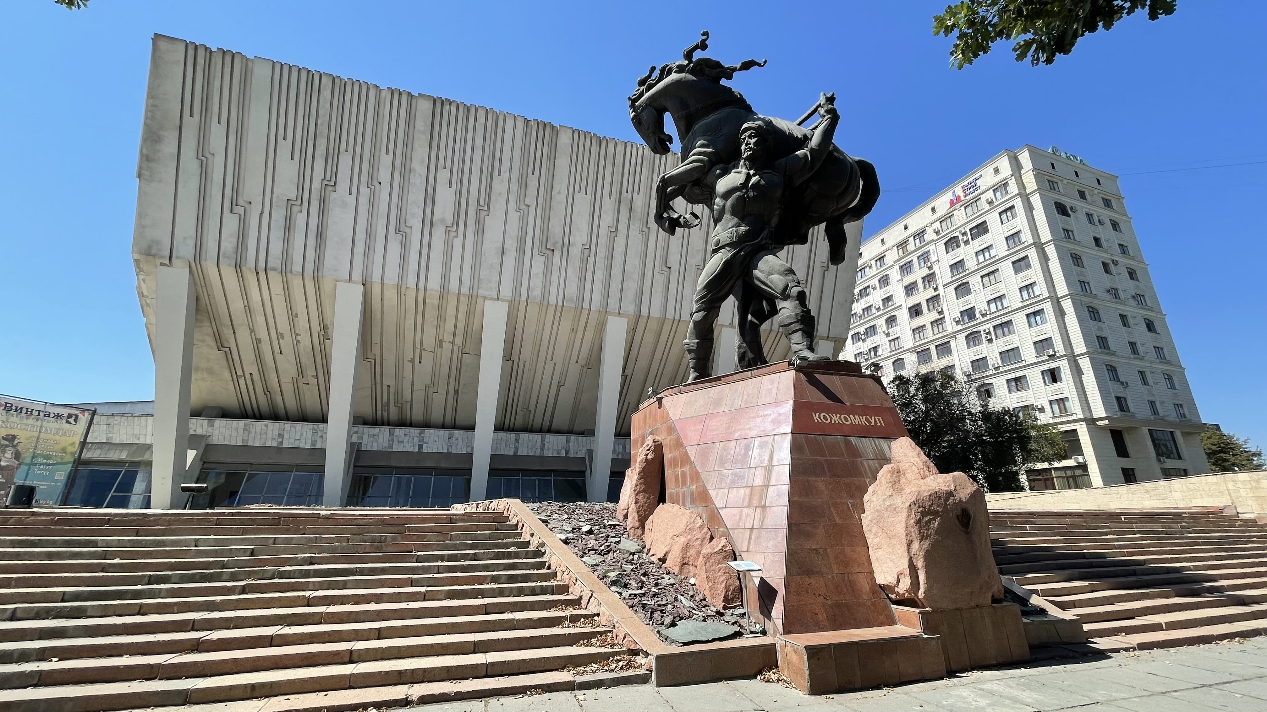 Soviet-era Sports Palace in Bishkek with the Kojomkul strongman statue in front, showcasing white marble architecture and monumental design in Kyrgyzstan