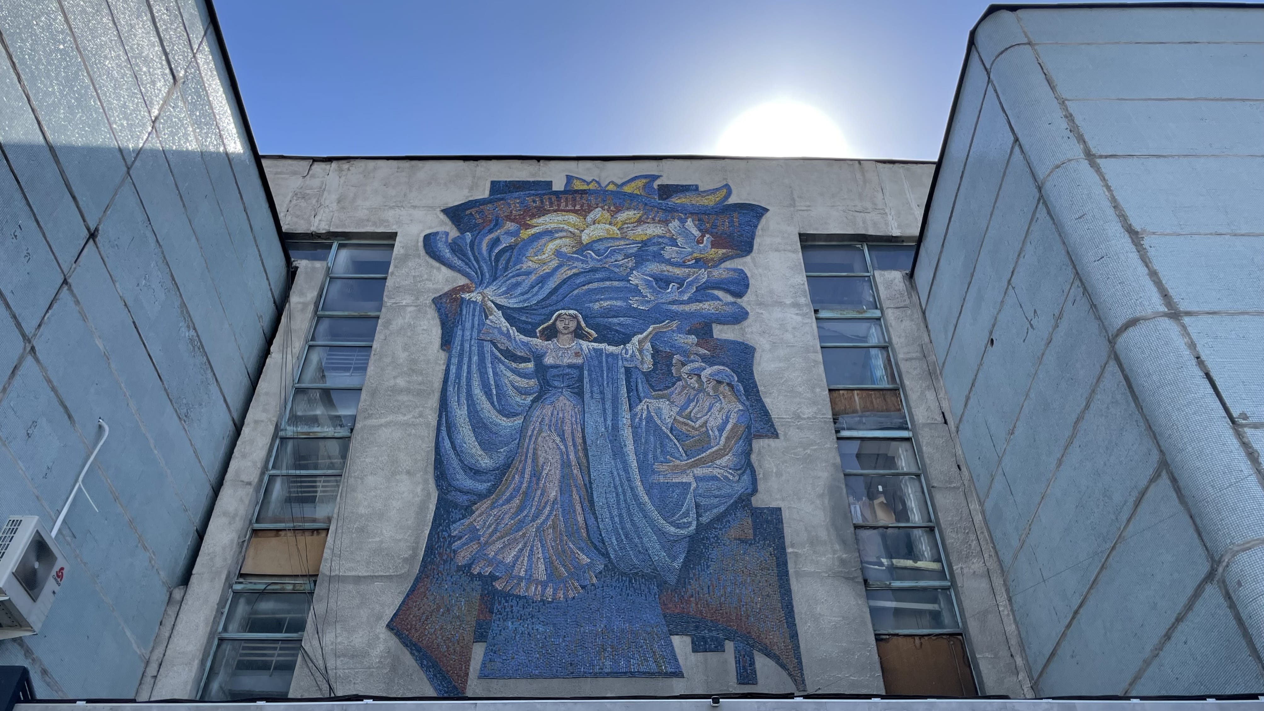 Large Soviet-era mosaic mural on a building in Bishkek, Kyrgyzstan, showing a blue-robed figure and symbolic imagery during 7 days in Kyrgyzstan.