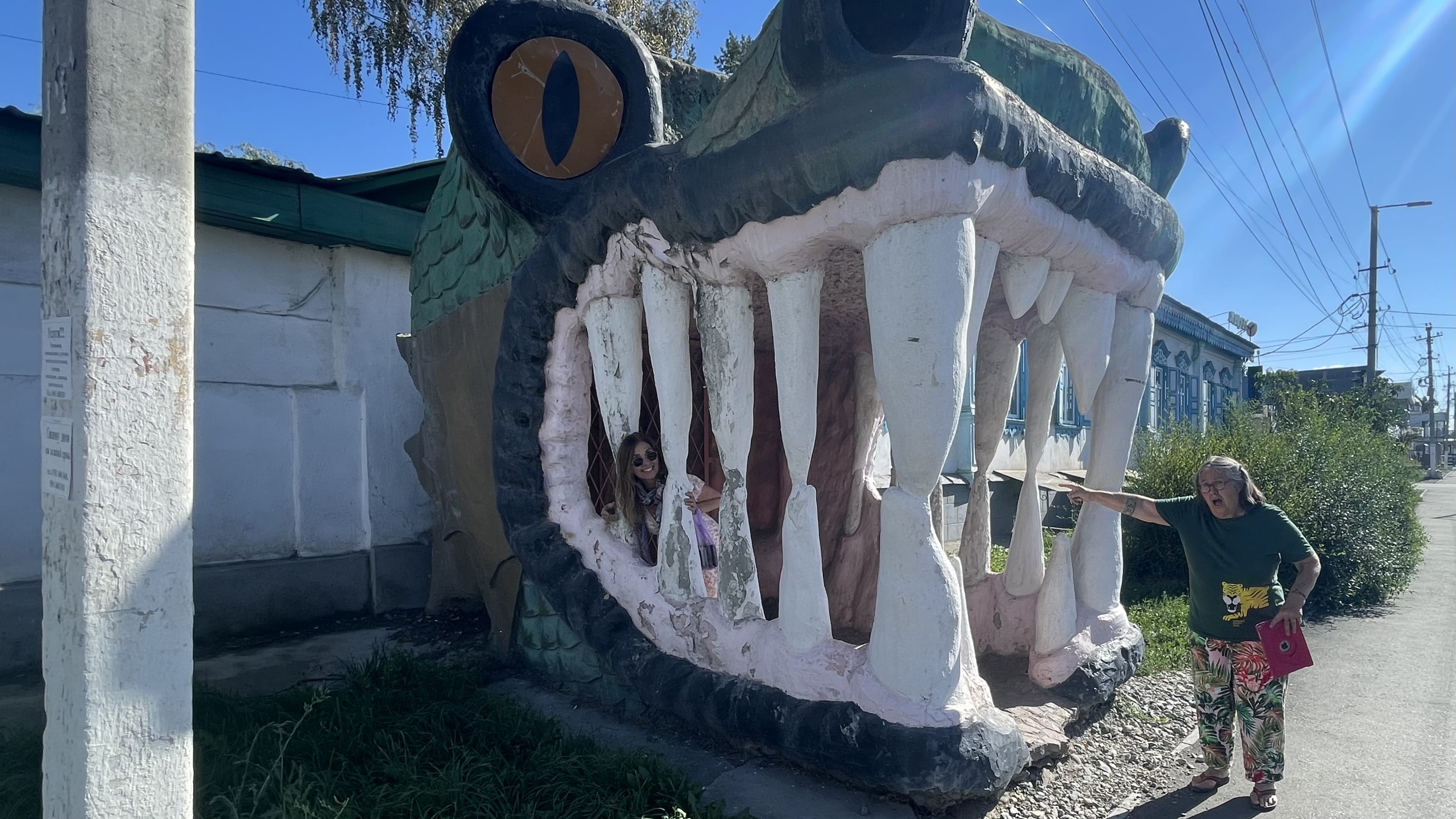 Large alligator sculpture in Karakol, Kyrgyzstan, with people standing inside its open mouth along a quiet street
