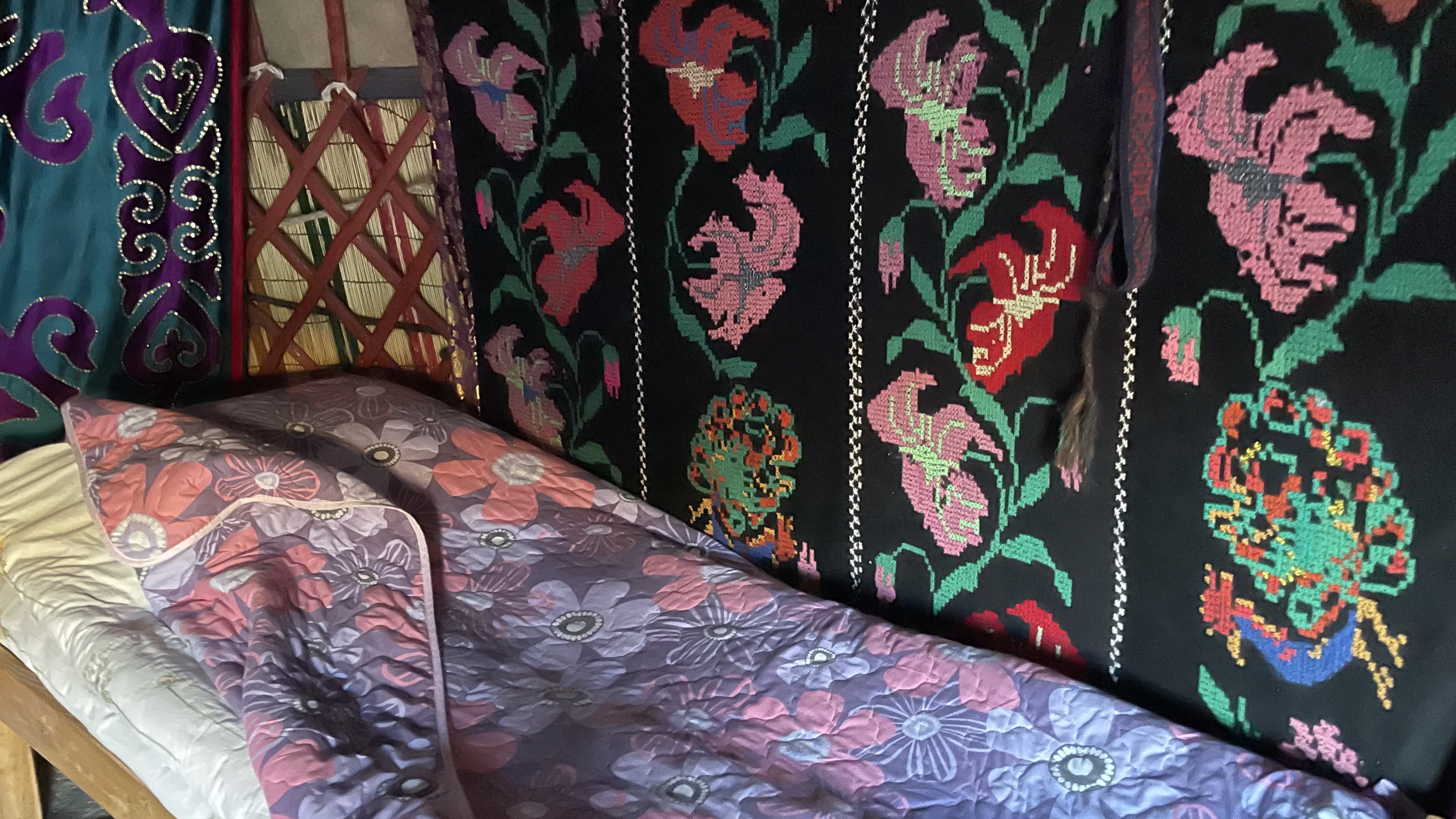 Interior of a traditional Kyrgyz yurt with colorful embroidered wall hangings and a quilted sleeping area