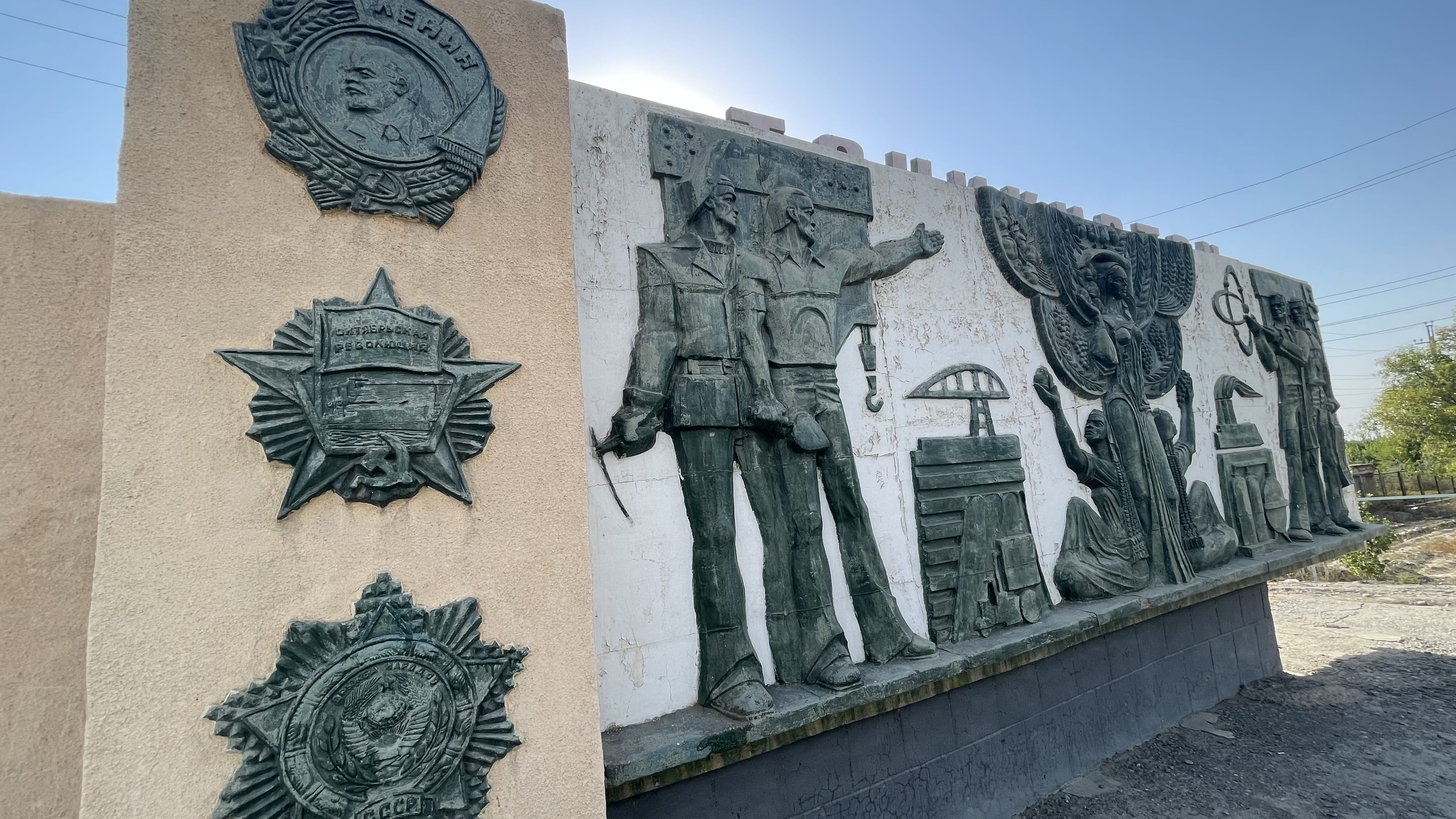 Soviet-era relief mural at the Uzbekistan–Tajikistan border near Oybek, depicting workers, soldiers, medals, and industrial symbols during a 3 days in Khujand, Tajikistan itinerary.