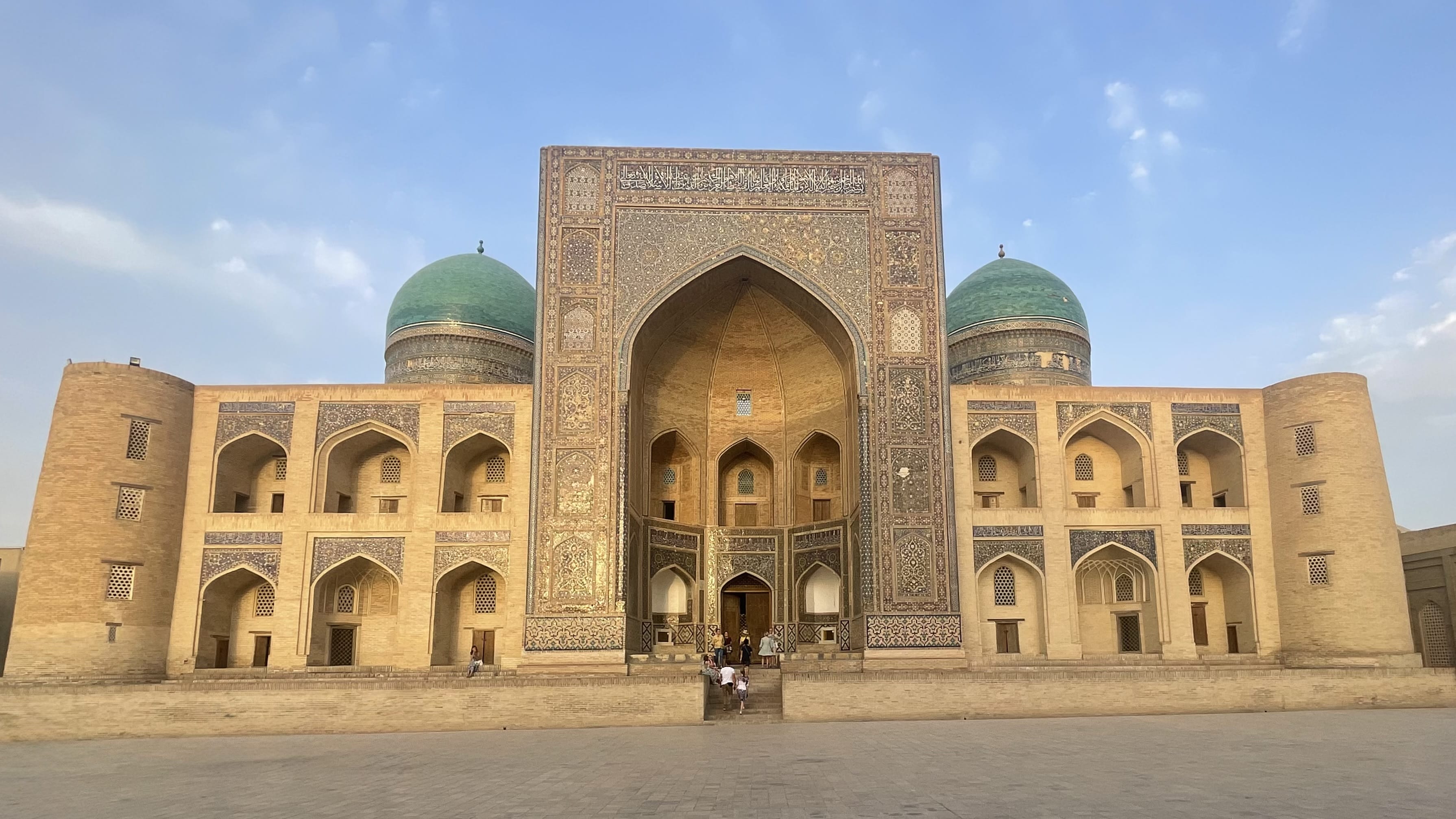 Ornate arched entrance of the Kalyan Mosque in Bukhara, Uzbekistan, with patterned tilework and people at the steps, on a 4 days in Uzbekistan trip.
