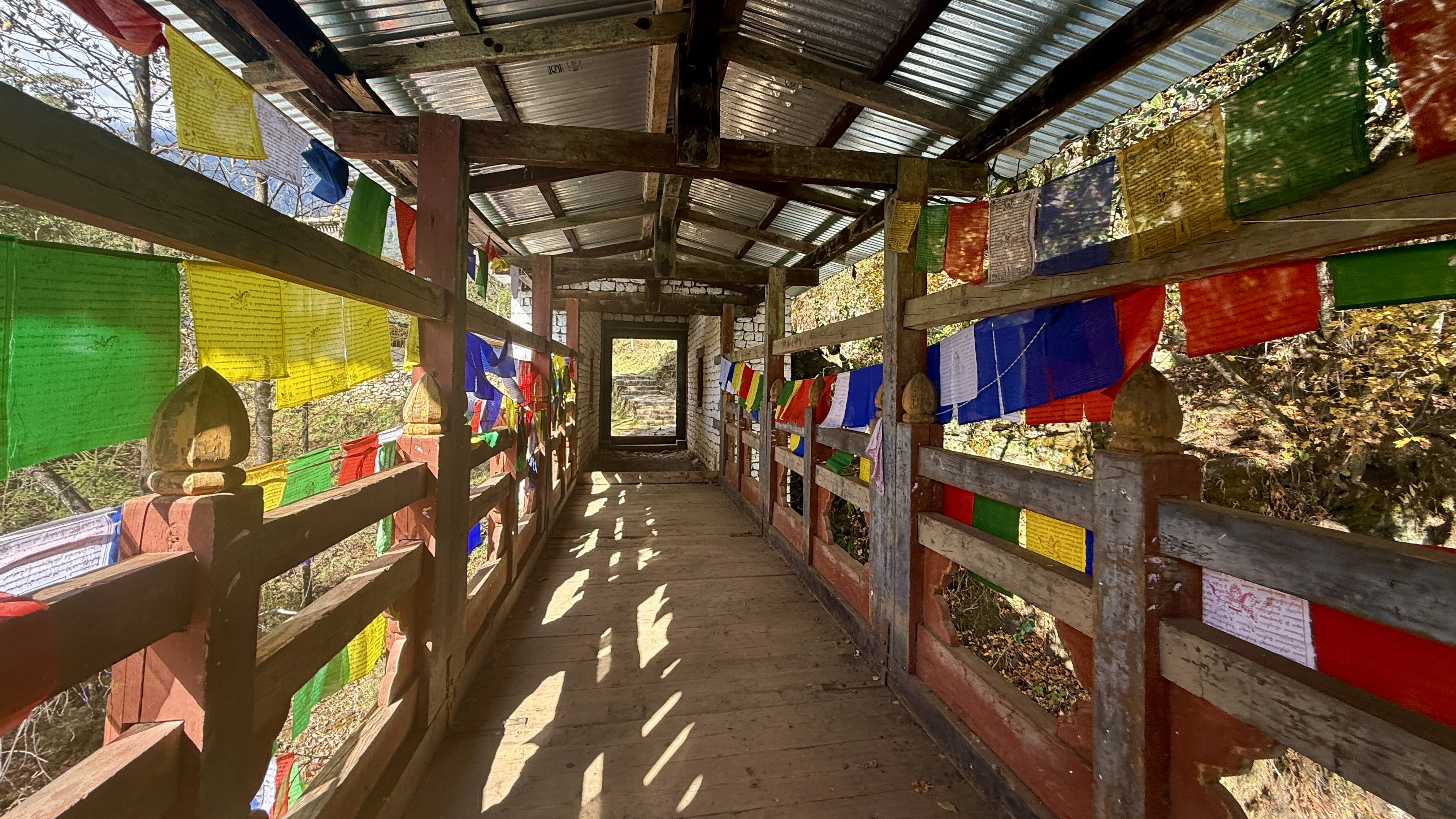 Covered wooden bridge lined with colorful prayer flags on the path leading to Cheri Monastery near Thimphu, Bhutan.