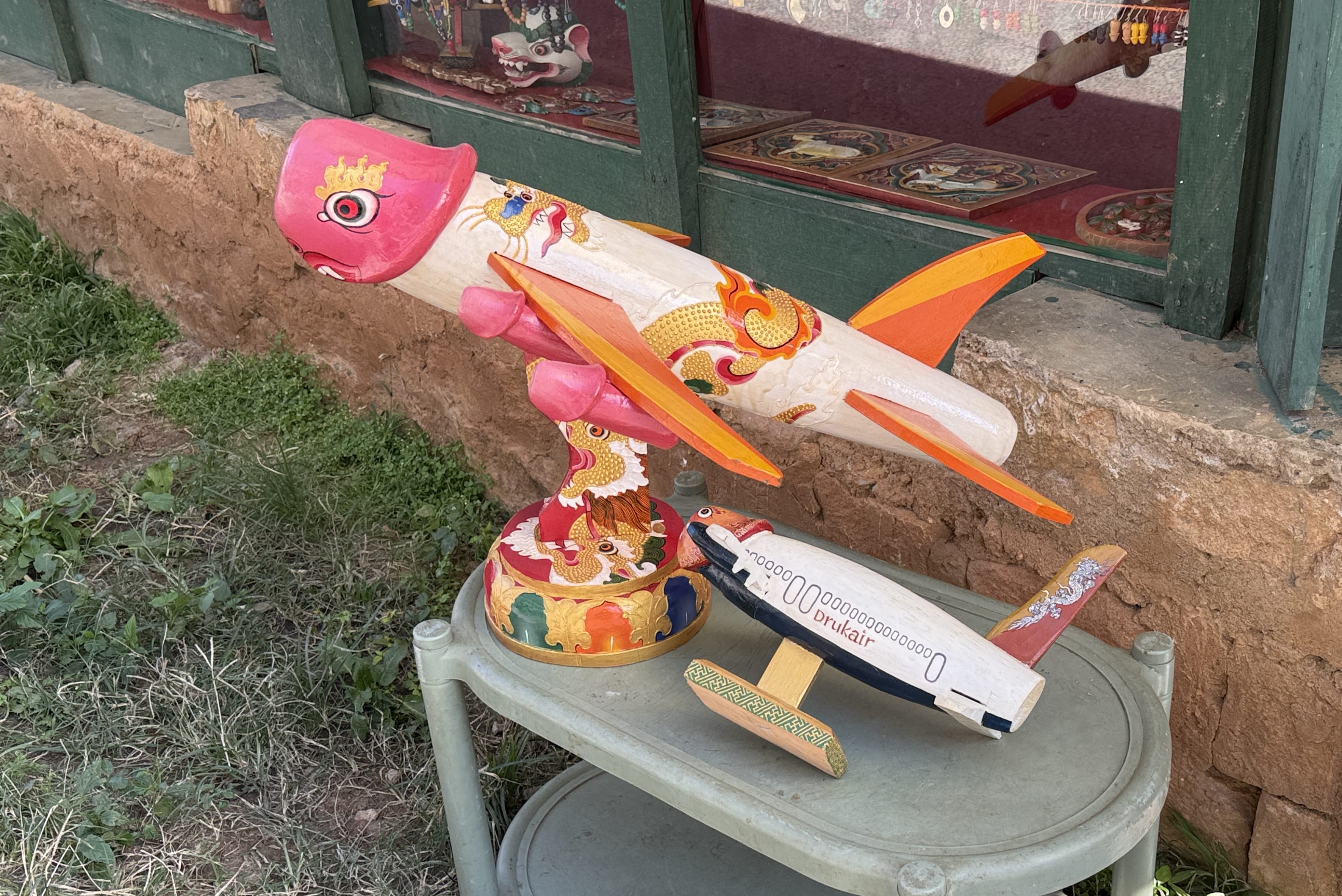 Colorful wooden folk sculptures, including a dragon-shaped airplane and a Drukair jet, displayed outside a shop near Chimi Lhakhang in Bhutan during an 11-day trip.