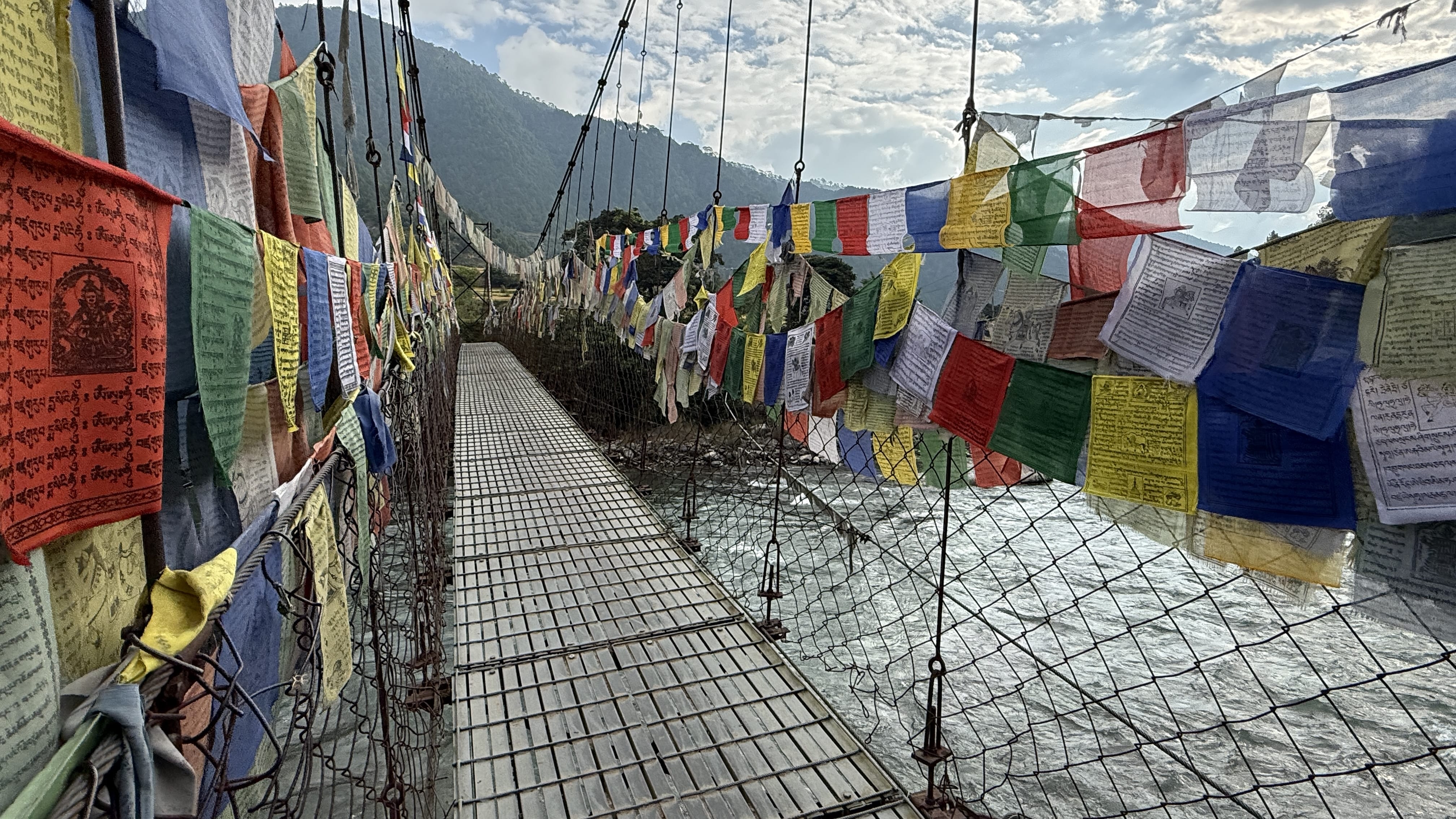 Suspension footbridge over the Mo Chhu River in Punakha Valley, Bhutan, lined with colorful prayer flags on the walk to Khamsum Yulley Namgyal Chorten