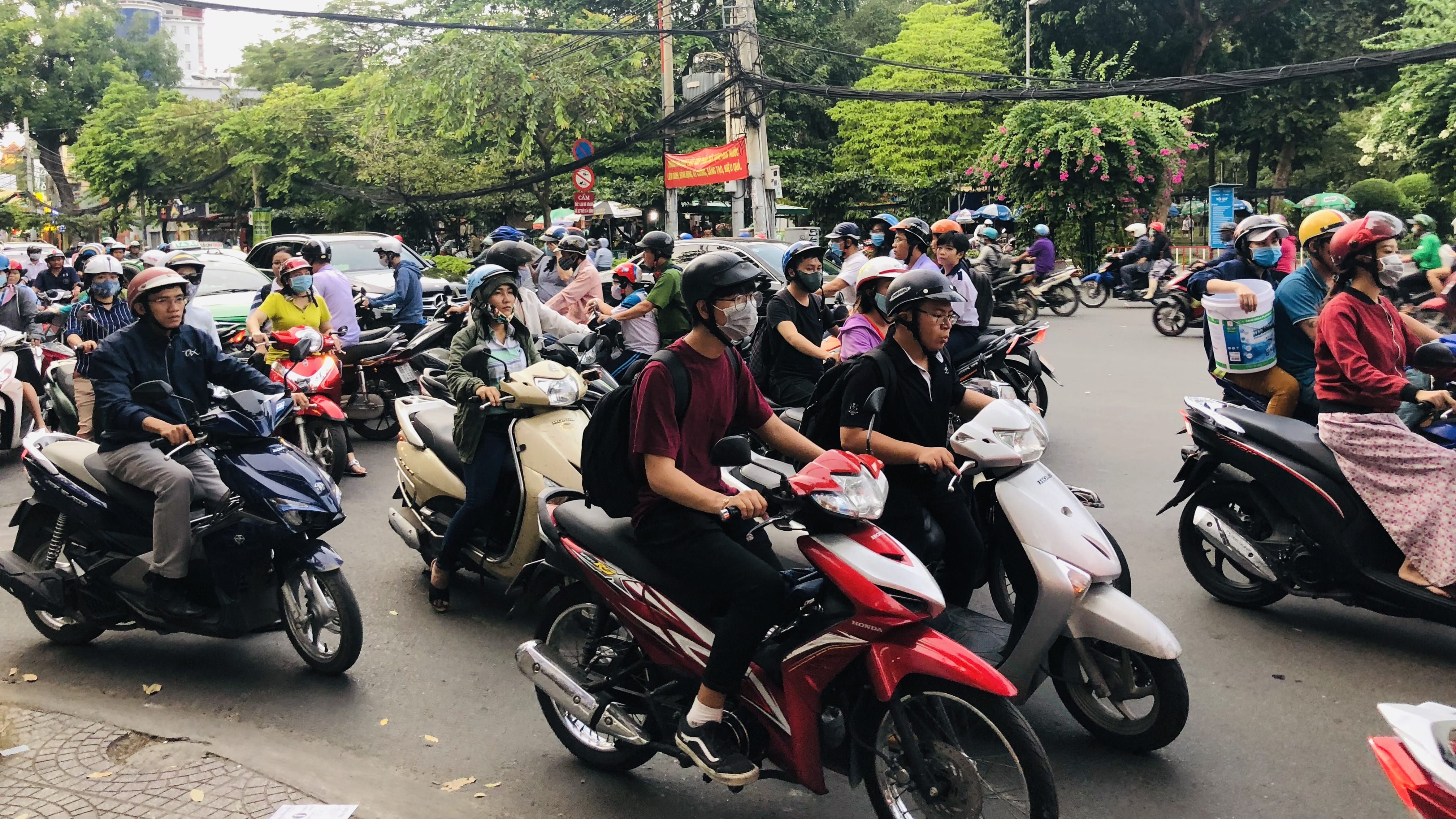 Busy intersection in Vietnam filled with motorbikes and scooter riders wearing helmets and masks during daytime traffic.